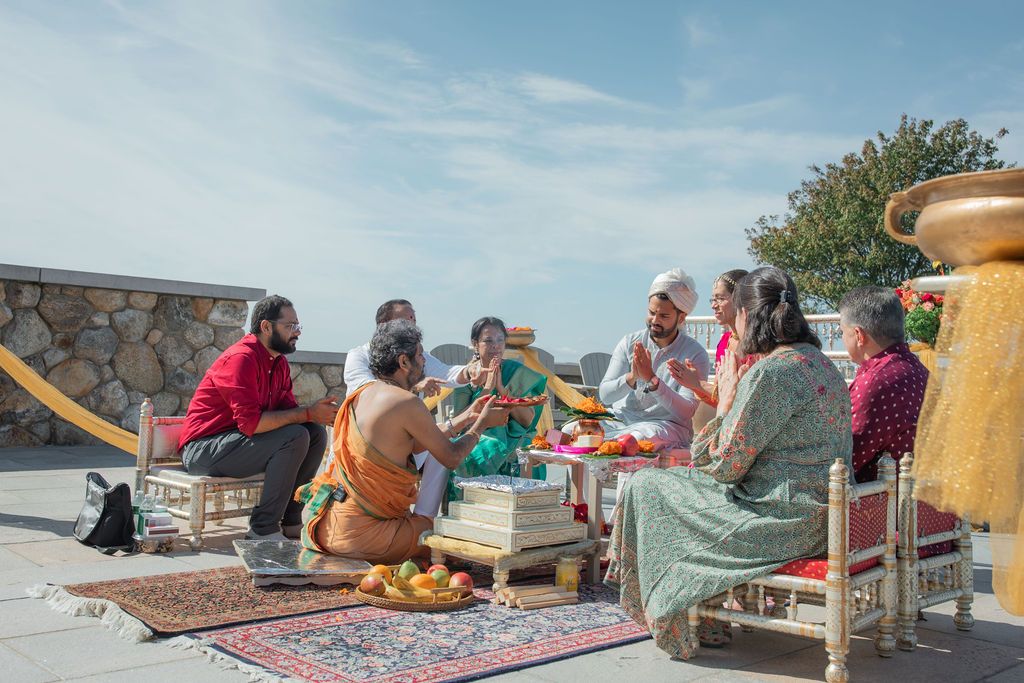 family sit around man praying at indian wedding ceremony