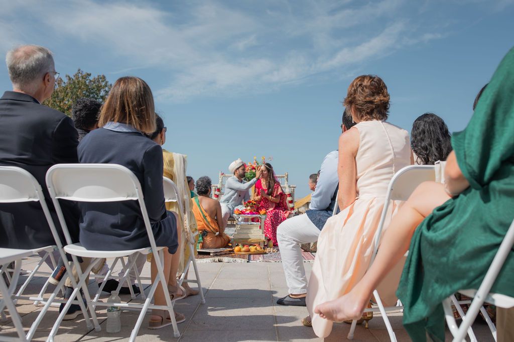 people sit in white folding chairs looking on to a traditional indian wedding ceremony