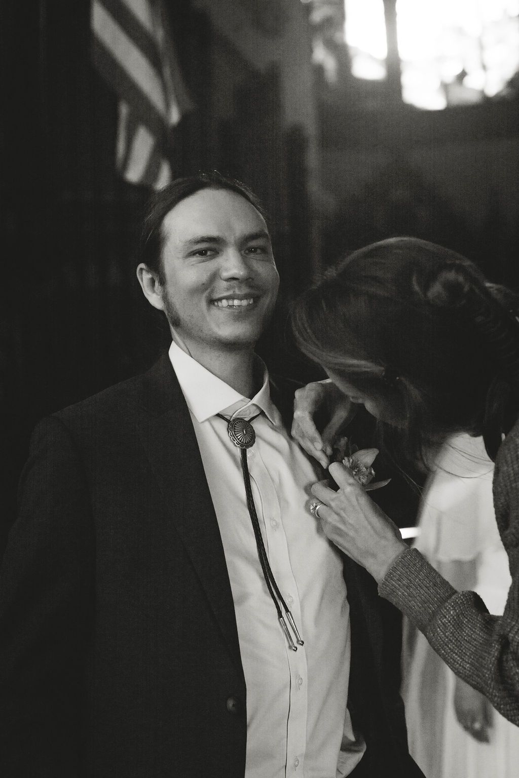A black and white photo of groom getting flowers pinned on his lapel
