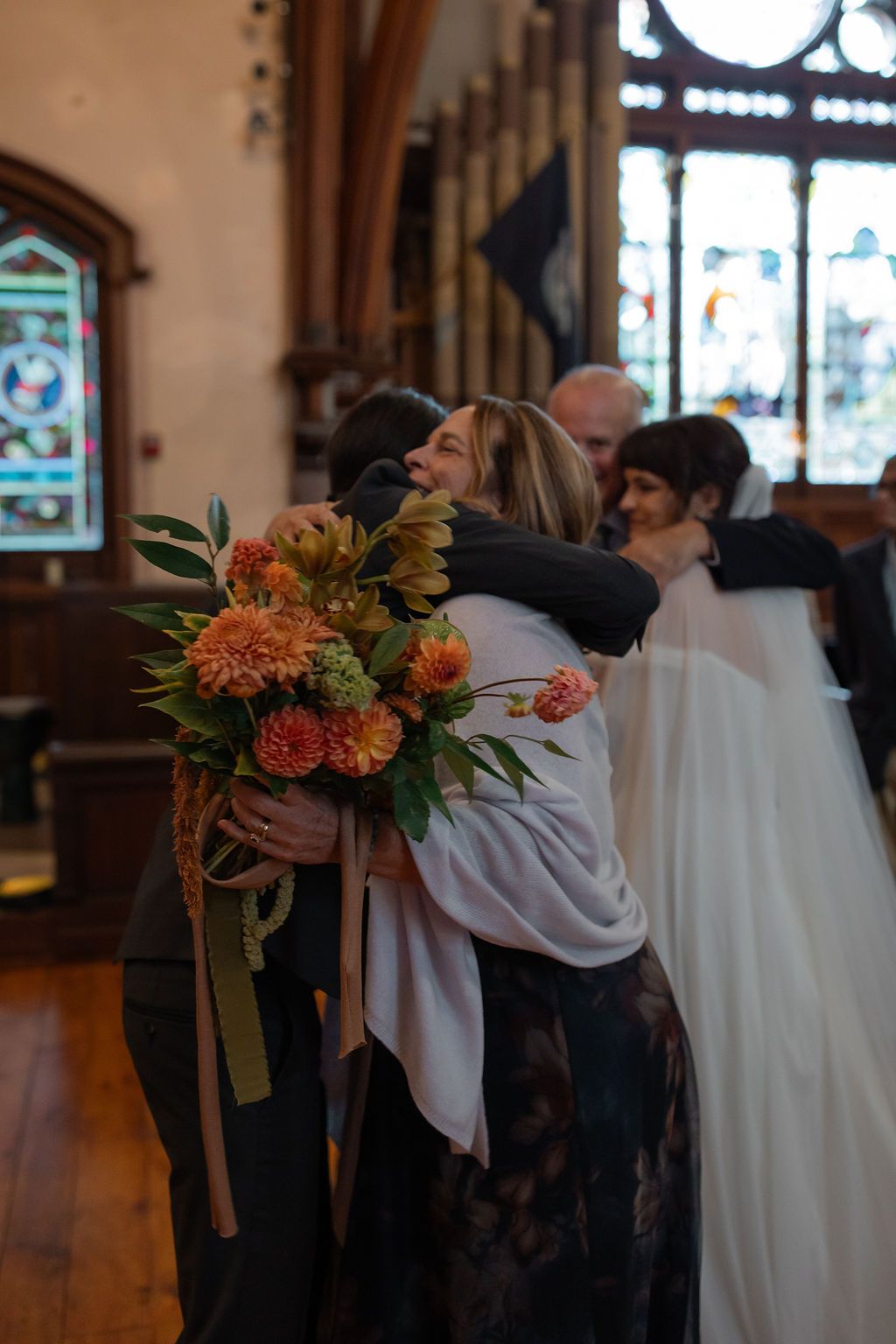 Bride shares embrace with her mom and dad inside of a church before getting married