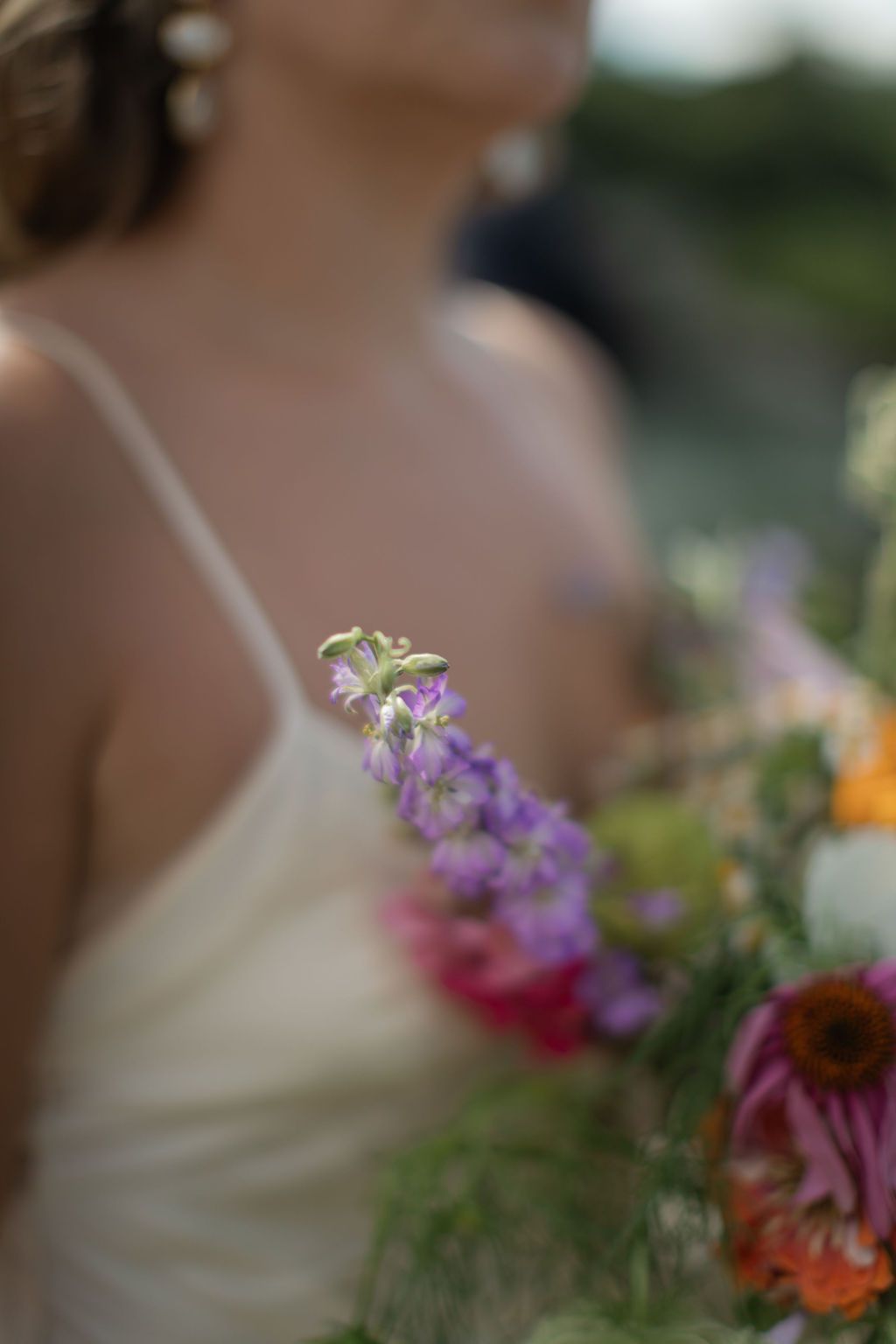 A delicate purple wildflower stem in focus with a soft-focus white dress and natural background.