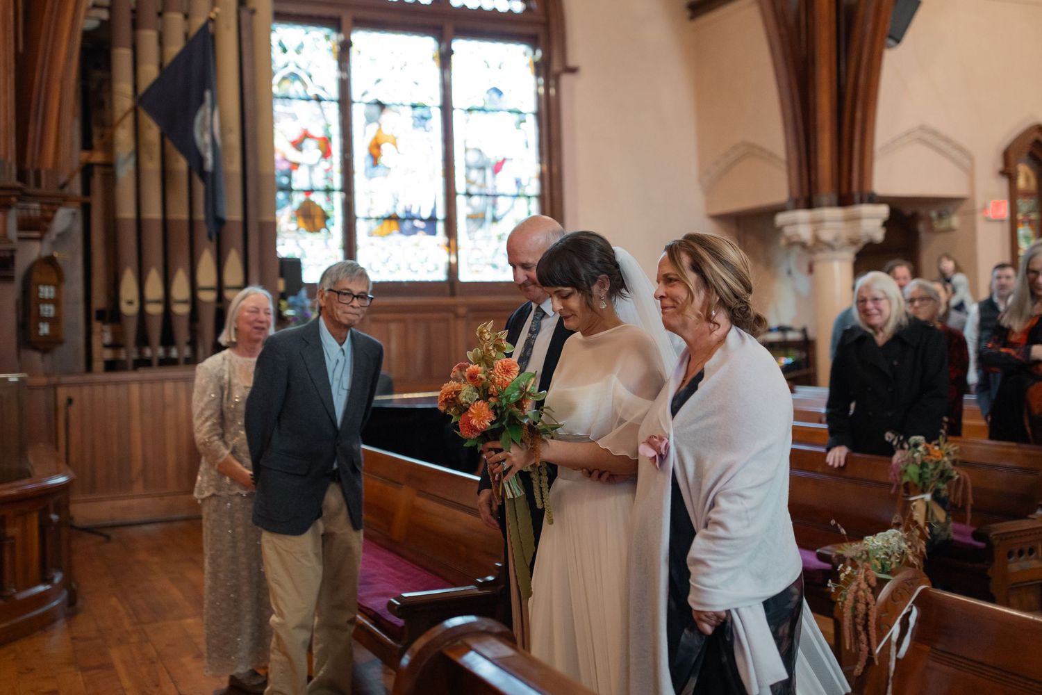 Wedding ceremony taking place in a traditional church with stained glass windows and wooden pews.