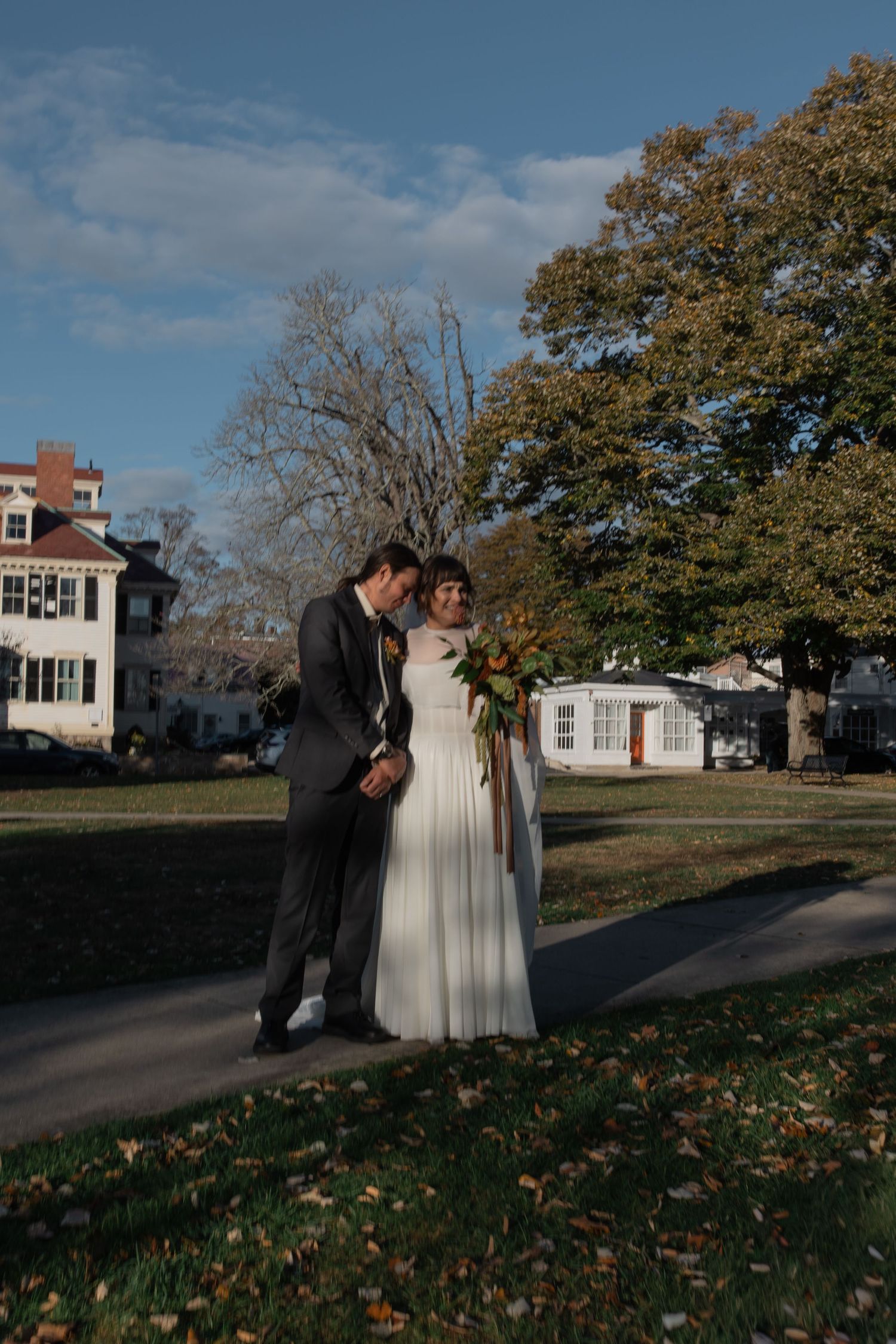 A couple in wedding attire poses for photos on an autumn day outside a white colonial-style house downtown Newport, Rhode Island