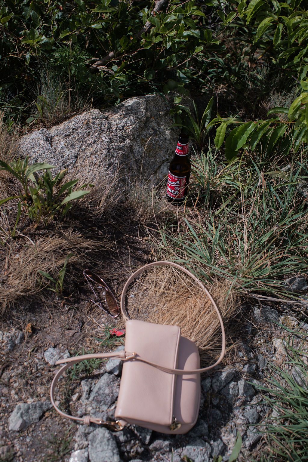 Pink leather handbag displayed on rocky surface against lush green foliage background.