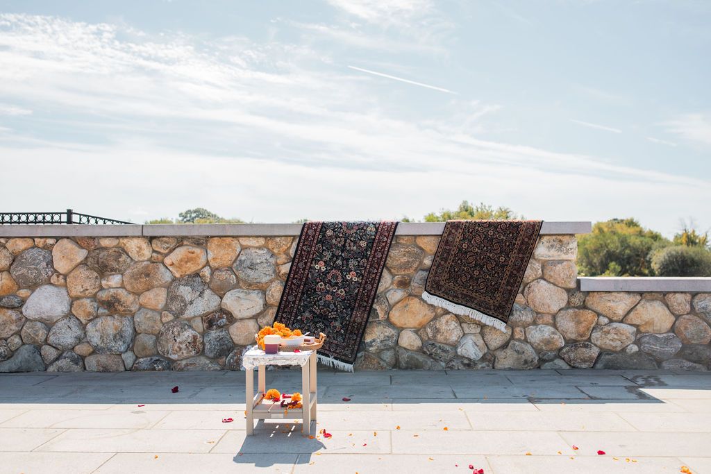 two decorative rugs hang on a stone wall on a sunny day