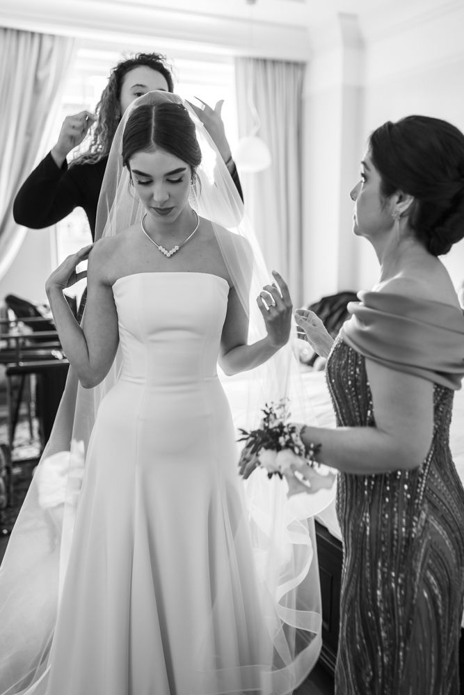 candid black and white photo of bride putting on her veil