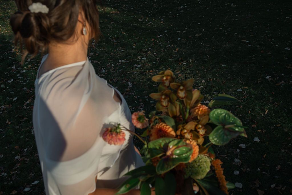 bride poses with autumn leaves and flowers against a dark background.