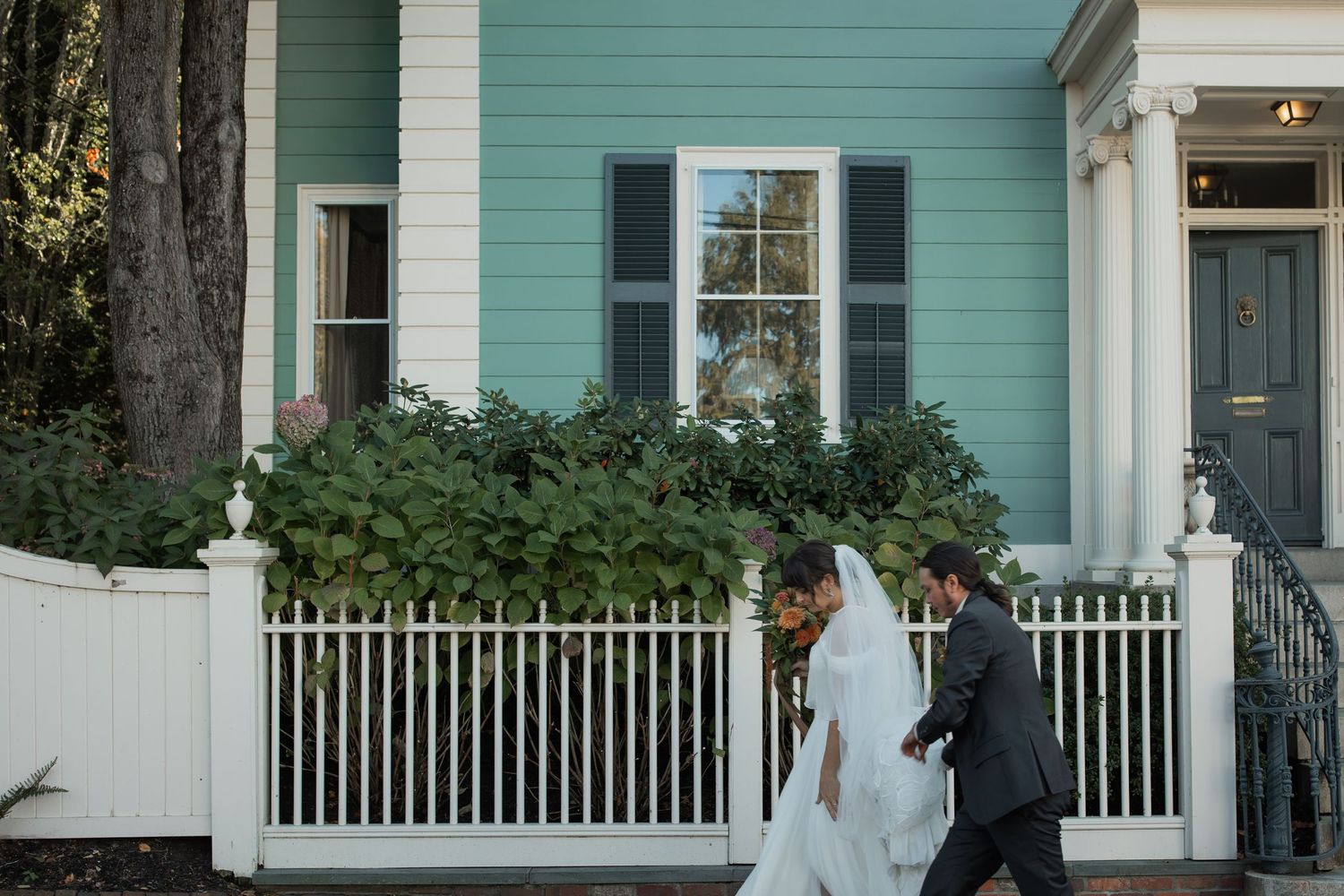 bride and groom walk together in front of a turquoise colored house