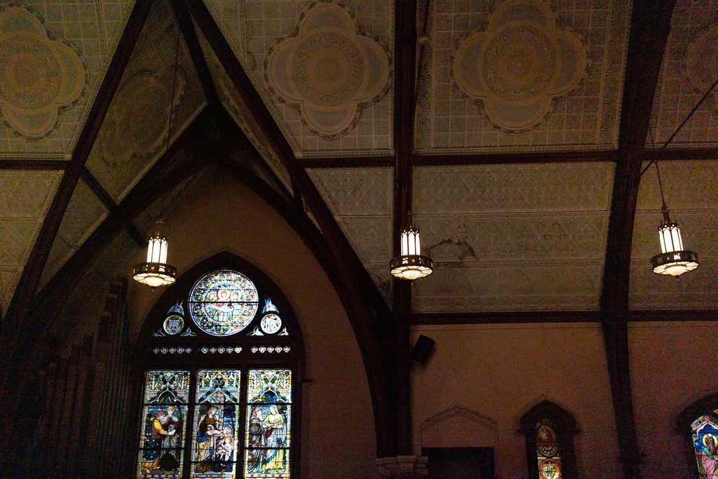 Ornate church interior with stained glass windows, wooden beams, and hanging pendant lights illuminating the sanctuary.