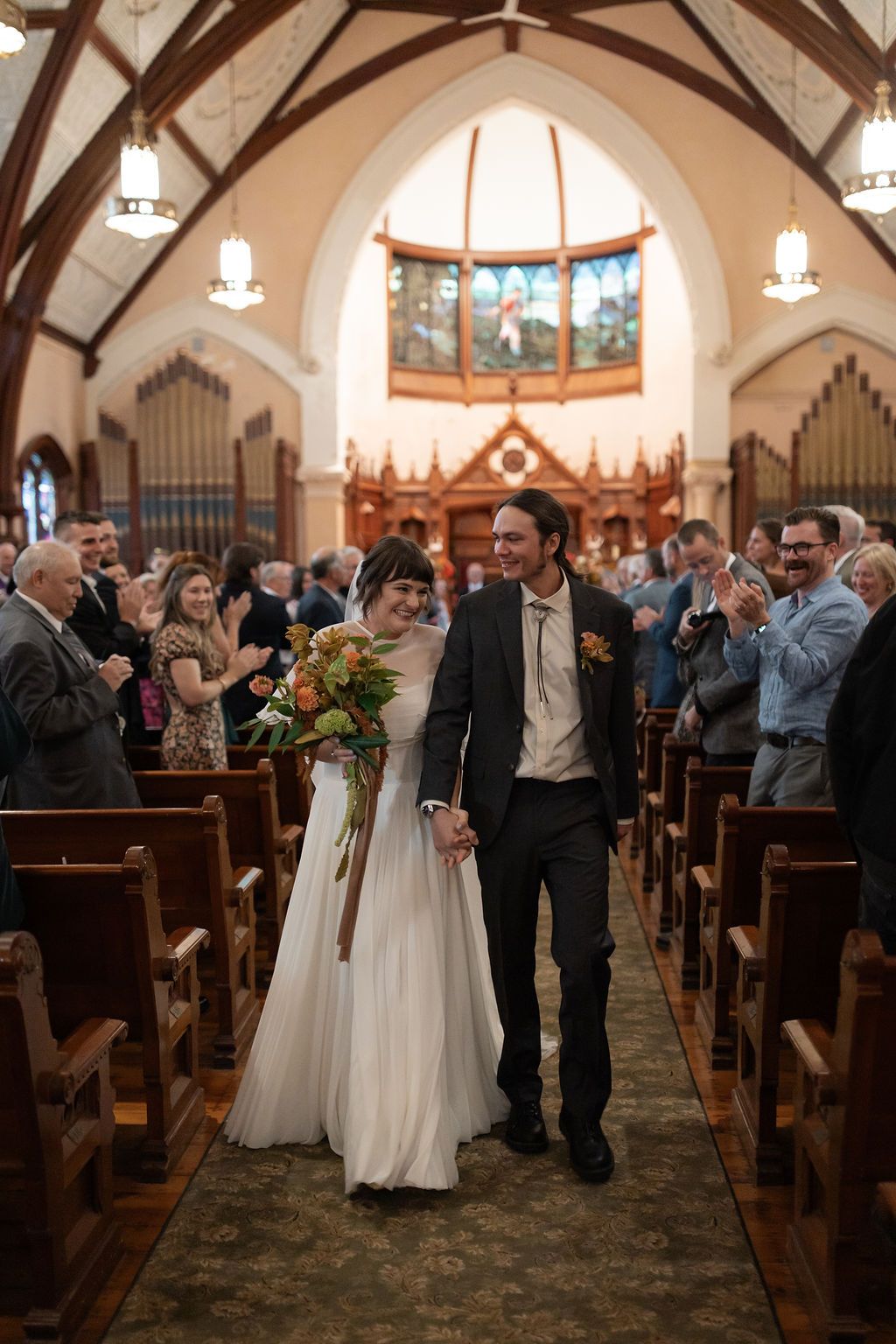 Bride and groom walk down the church aisle after ceremony as guests look on in a beautifully lit sanctuary.