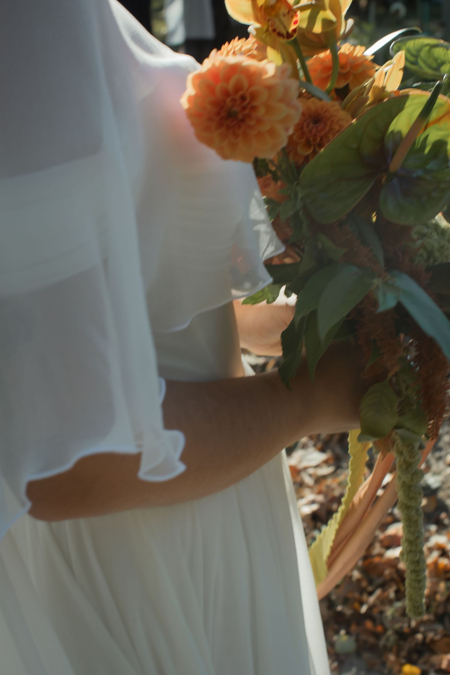 A white flowy dress is shown next to peach-colored dahlia flowers in soft natural lighting.