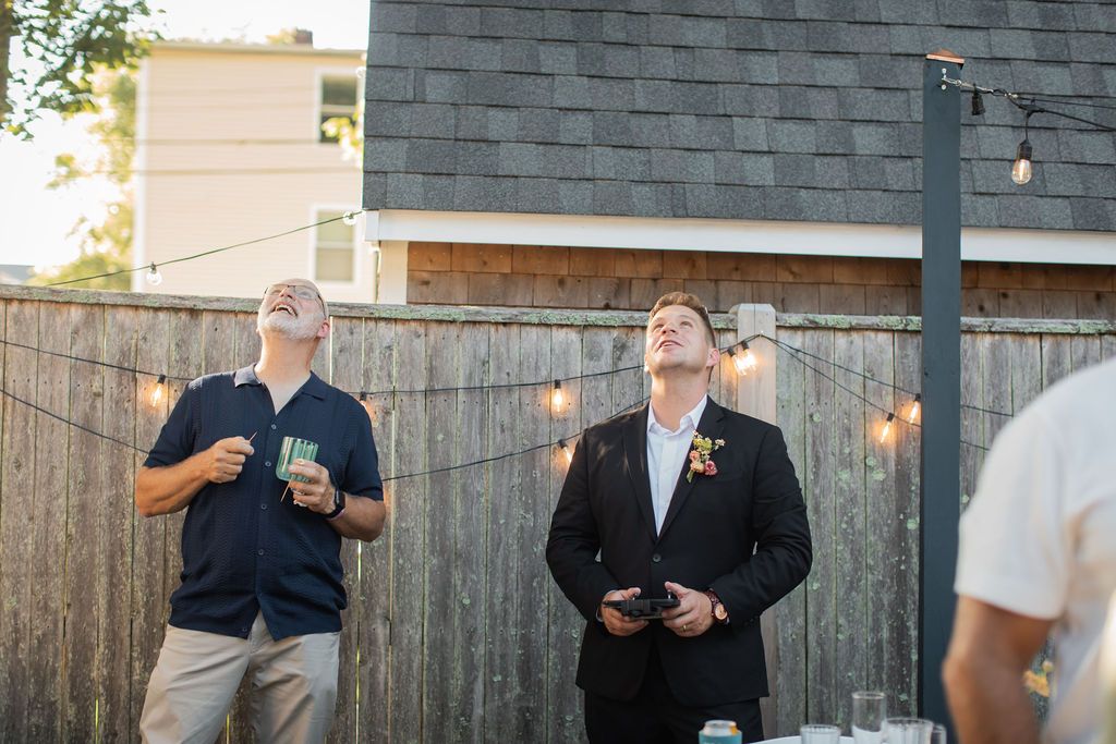 wedding guests look toward the sky in front of backyard fence
