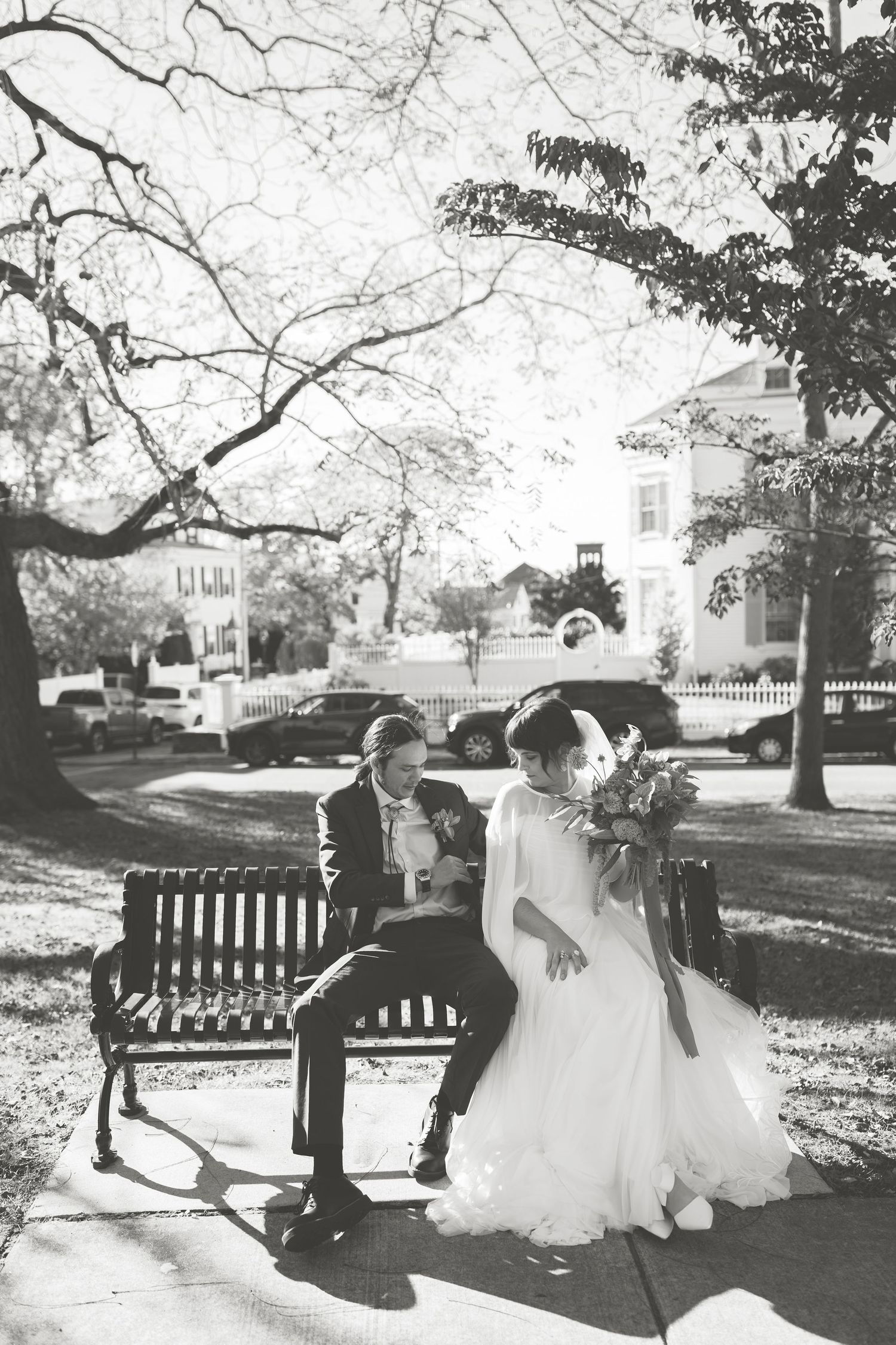 A couple sits together on a park bench in a romantic outdoor setting during their wedding portraits