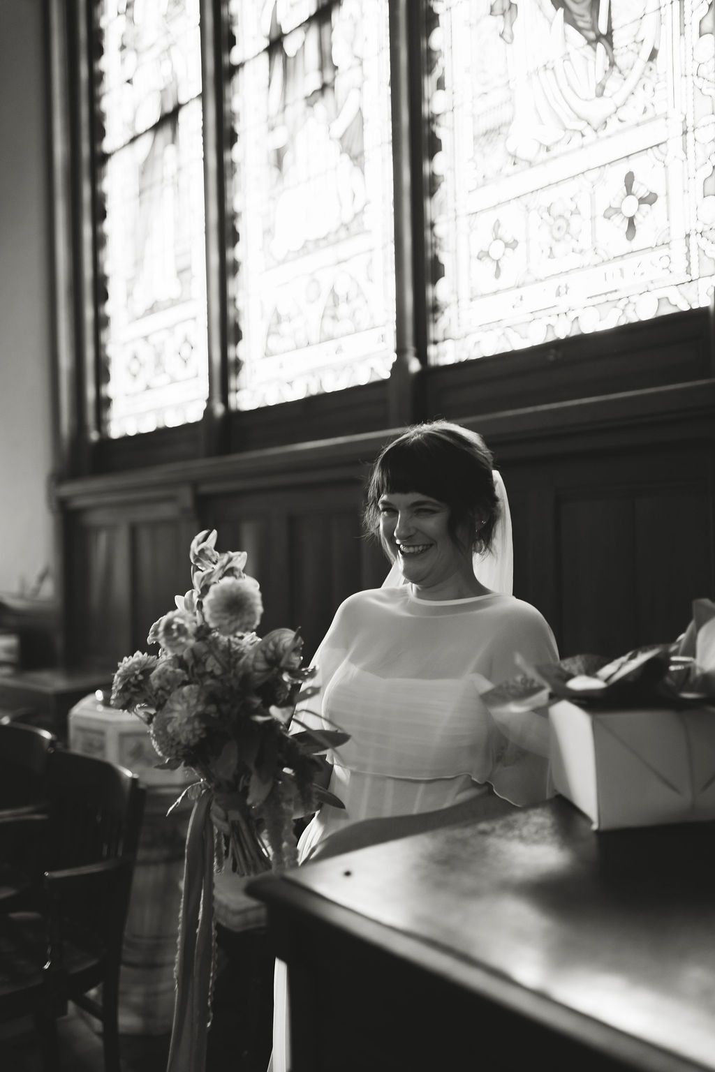 bride smiling standing by a window with flowers in soft natural light.