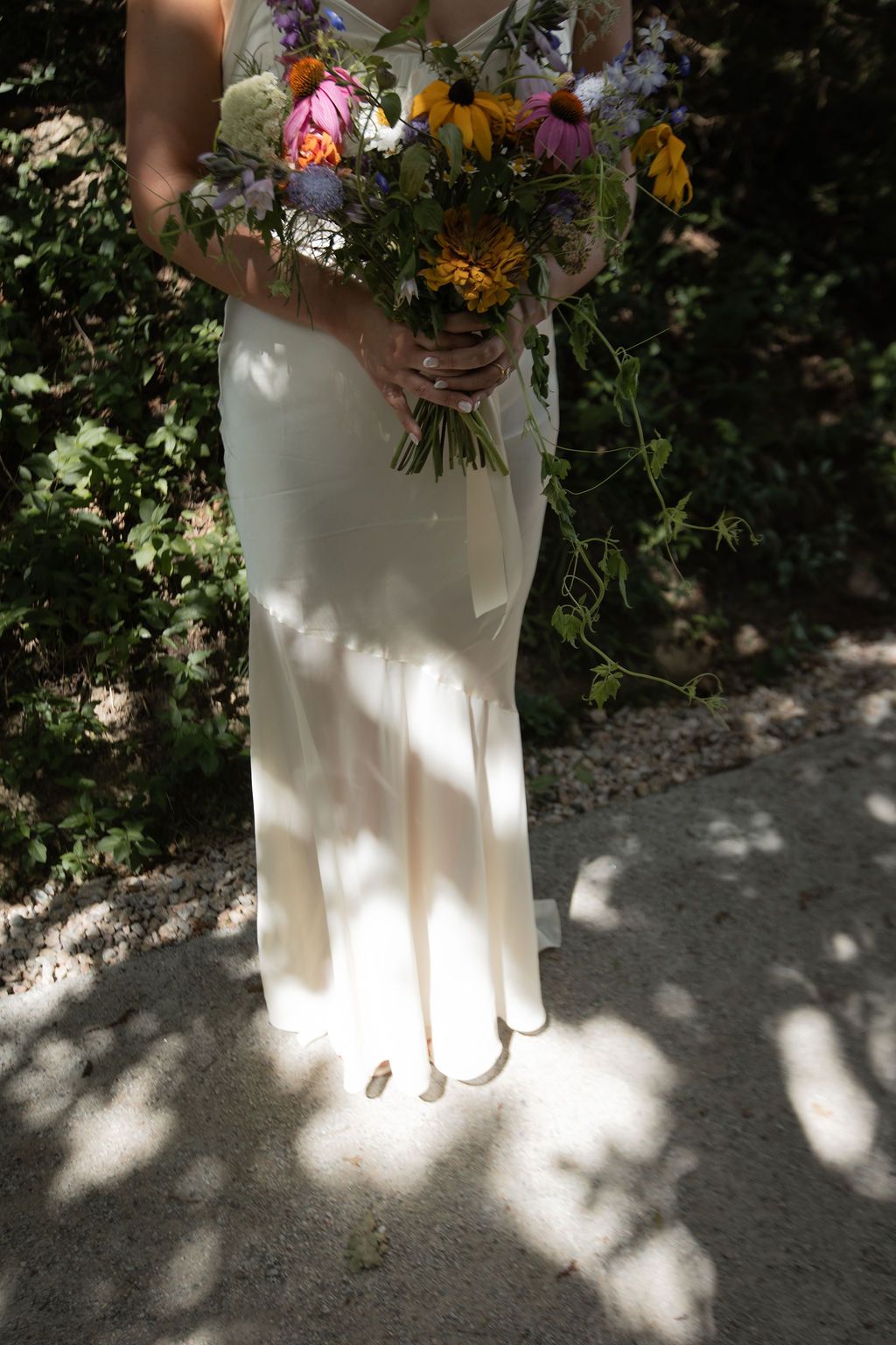 minimalist silk wedding dress in shadow of trees with wildflower bouquet
