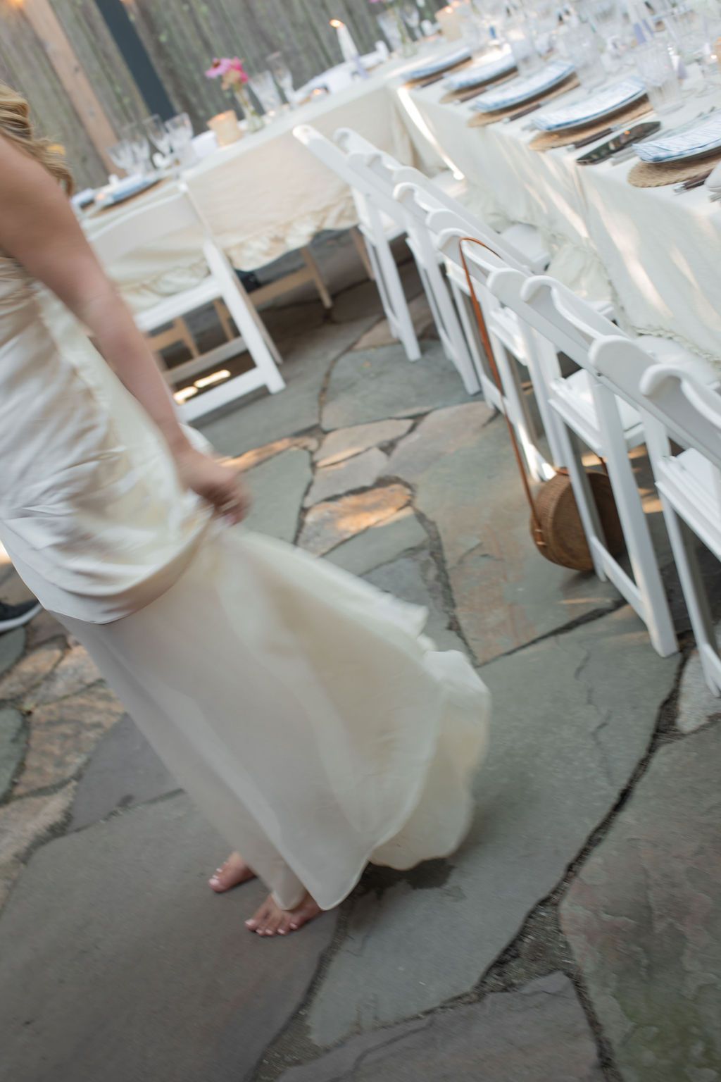 White dress flowing over stone patio floor with white chairs in background at outdoor event venue.