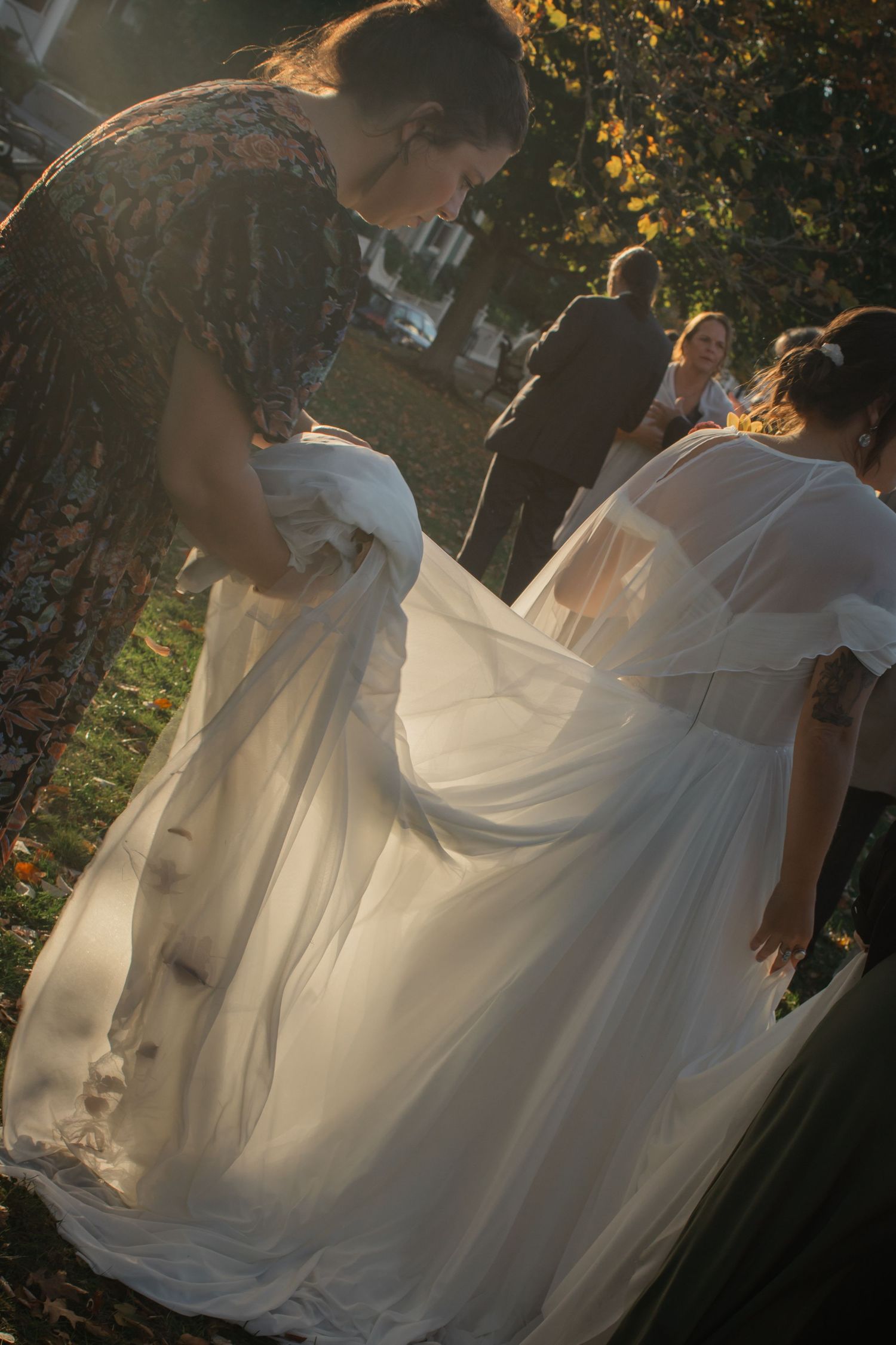 A bride's white wedding dress flows gracefully in the sunlight through trees during an outdoor photoshoot.