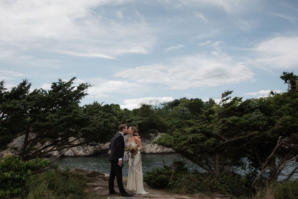 bride and groom kissing near trees rocks and ocean