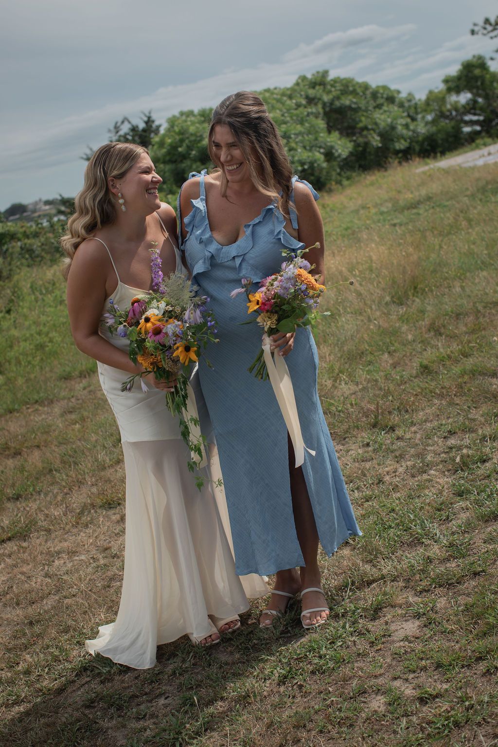 photo of bride and bridesmaid laughing together near the ocean