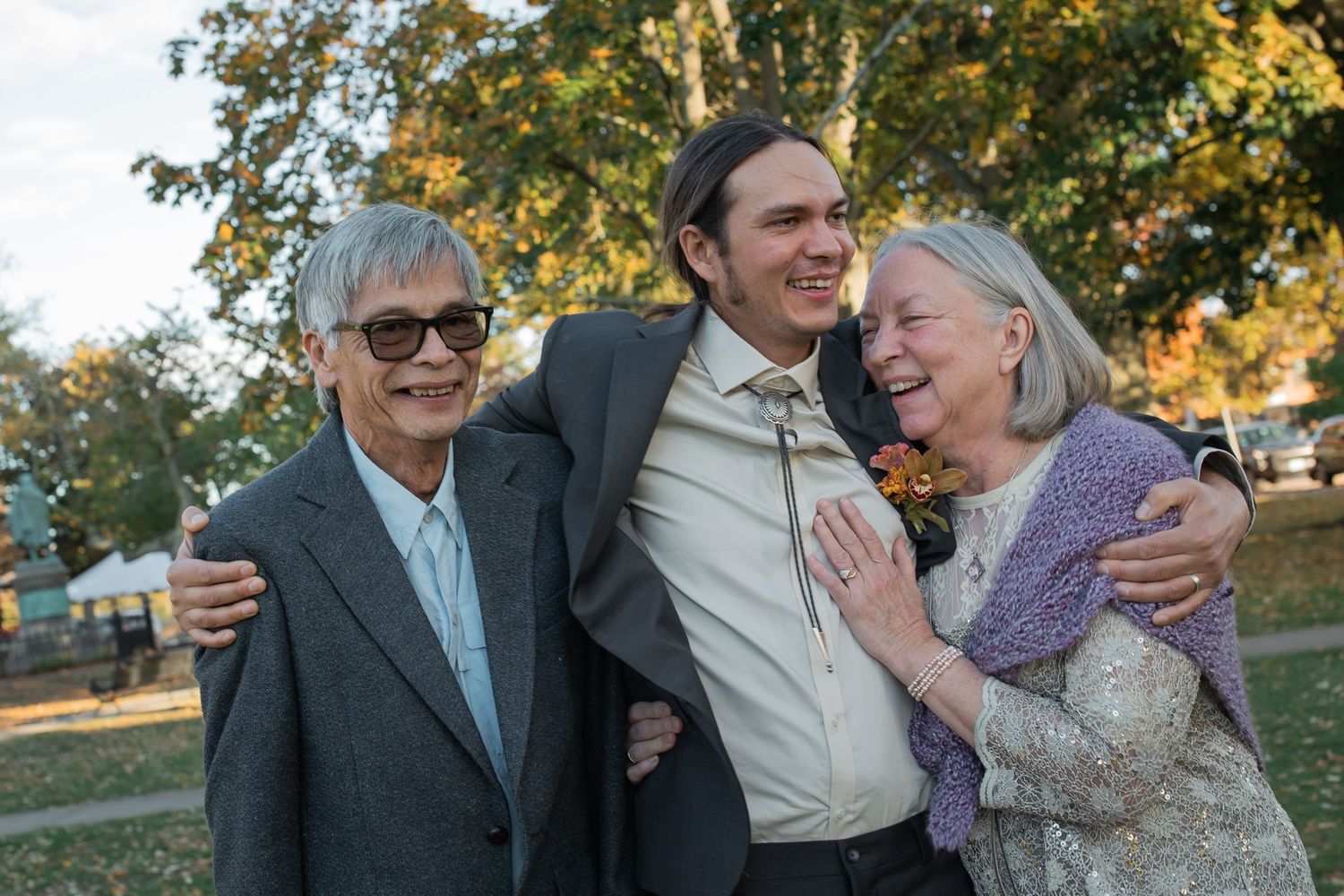 Family shares a joyful moment together outdoors during wedding golden hour with autumn trees in the background.