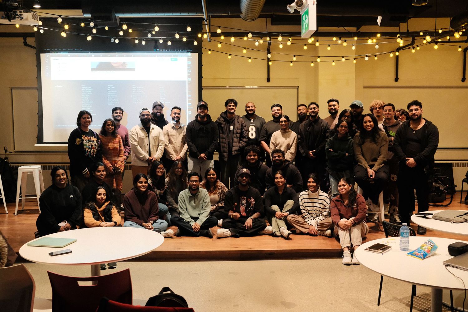 Large group photo of workshop participants in a conference room with string lights.