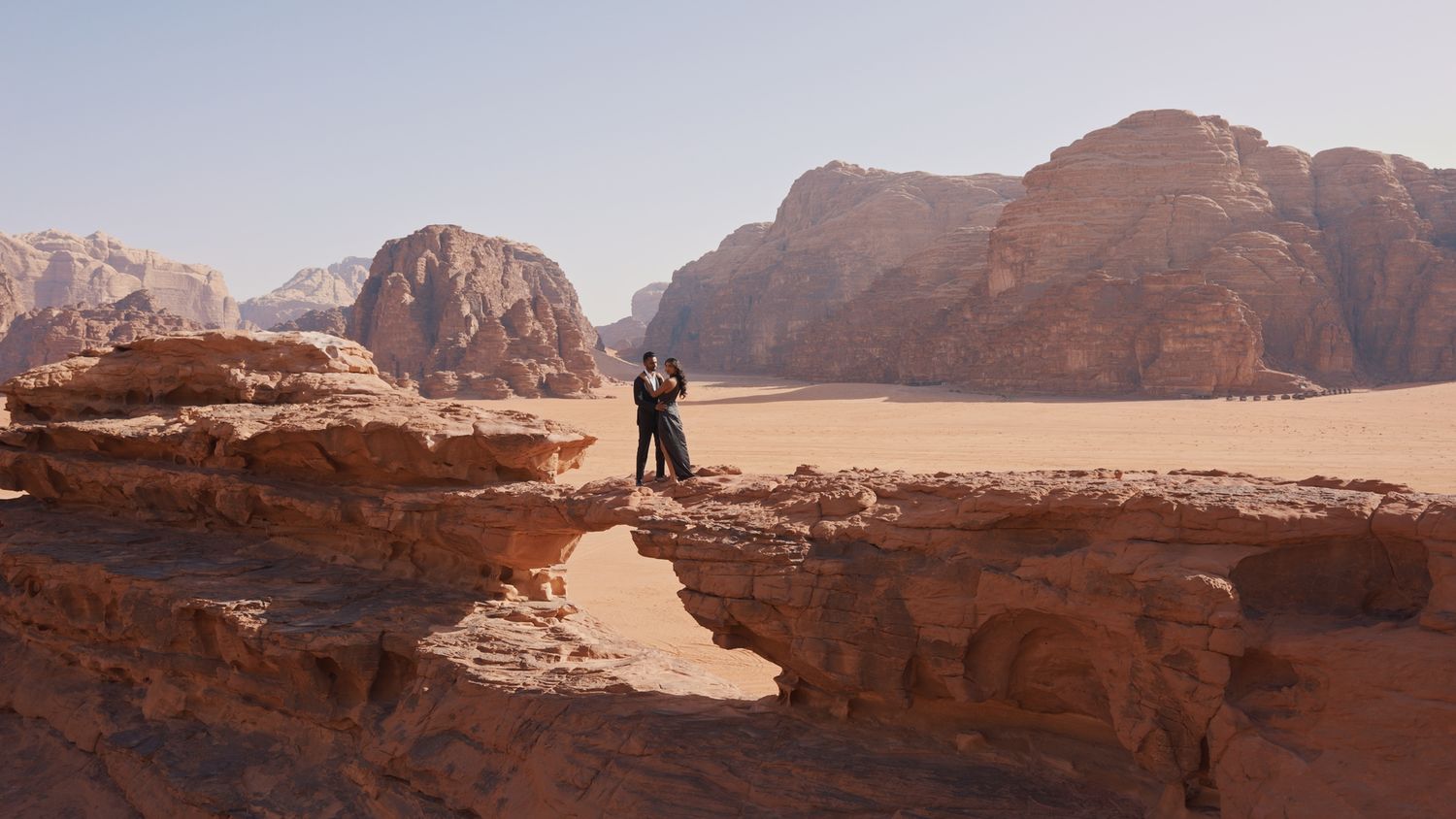 Rocky desert terrain with dramatic mountain formations against clear sky.