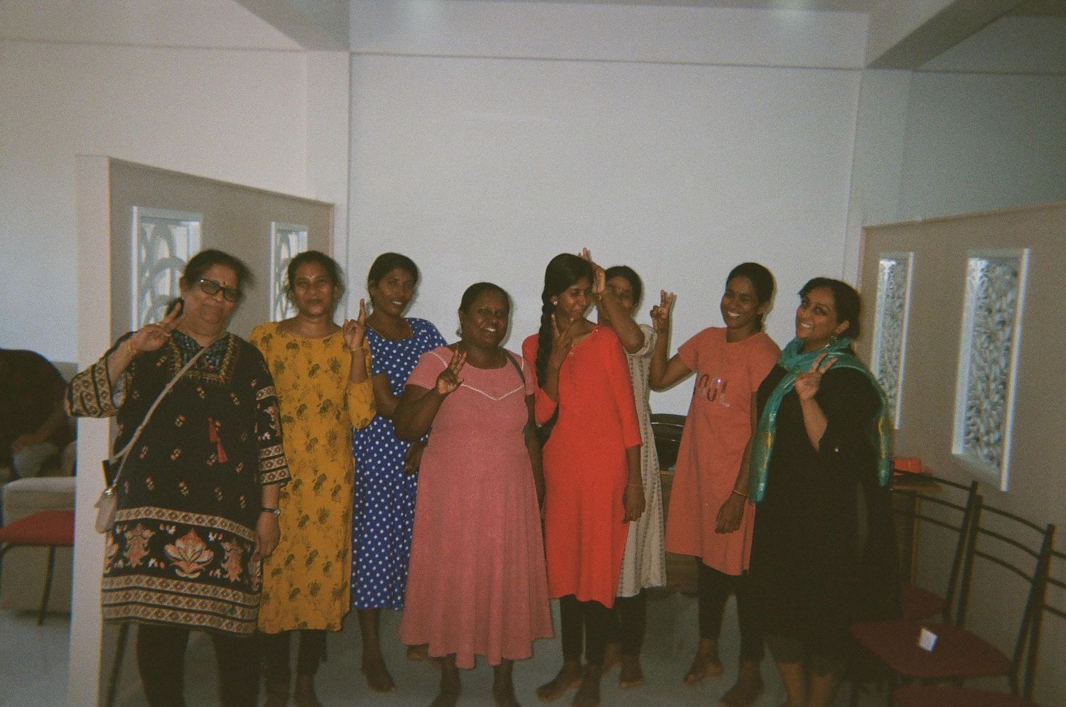 Group photo of people lined up against white wall in casual attire.