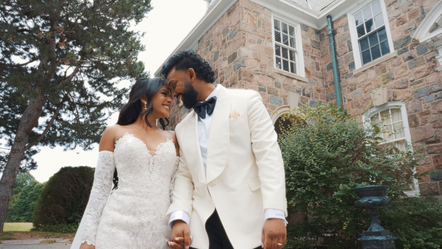 Elegant wedding couple shares intimate moments against a stone building backdrop.