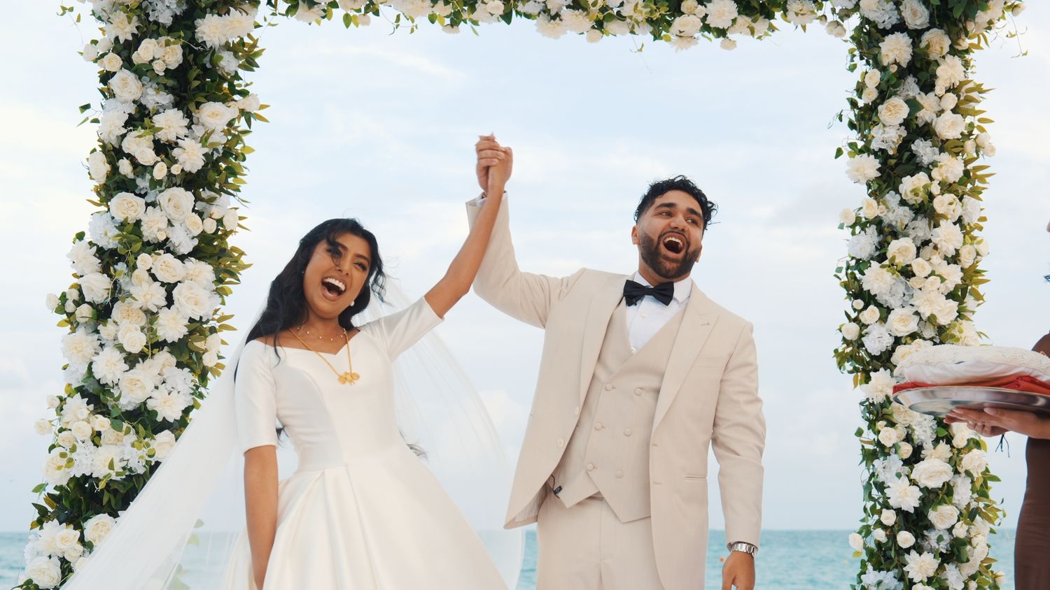 Beach wedding ceremony setup with white floral arch and ocean backdrop.