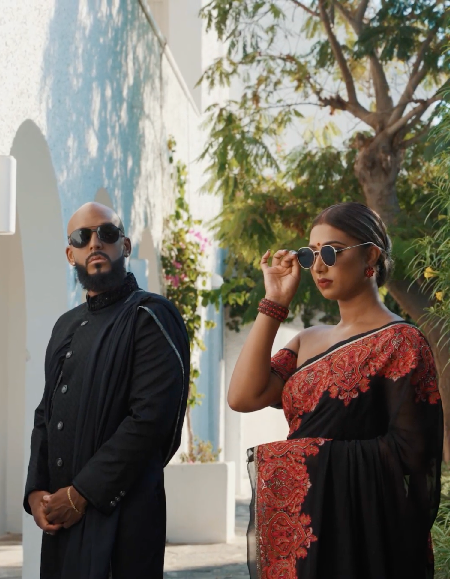 Stylish couple posing against white Mediterranean architecture with ocean views.