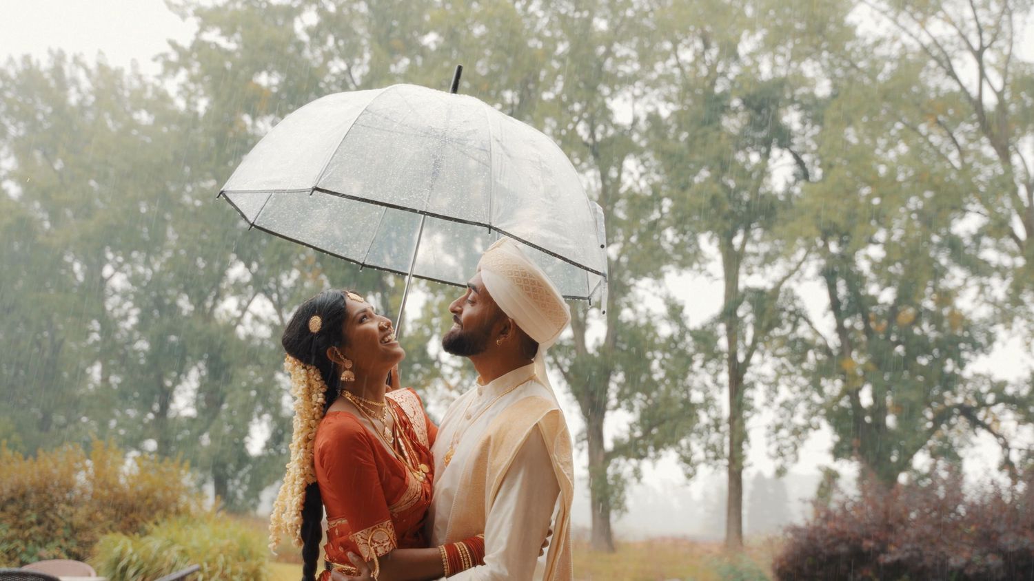 Wedding couple poses with white umbrella in outdoor garden setting.