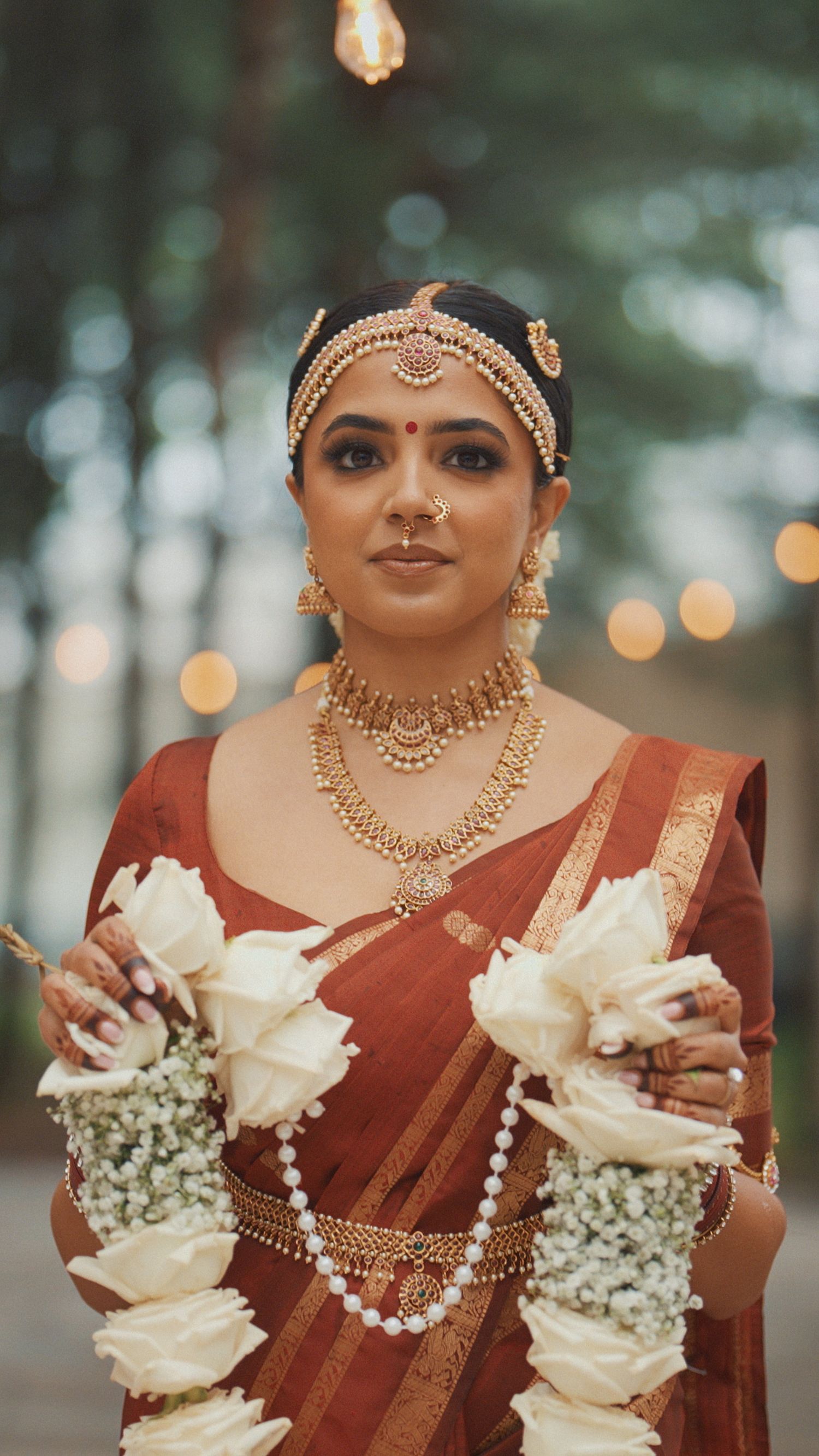 Close-up details of traditional Indian bridal jewelry and red sari with white floral accents and baby's breath bouquet.