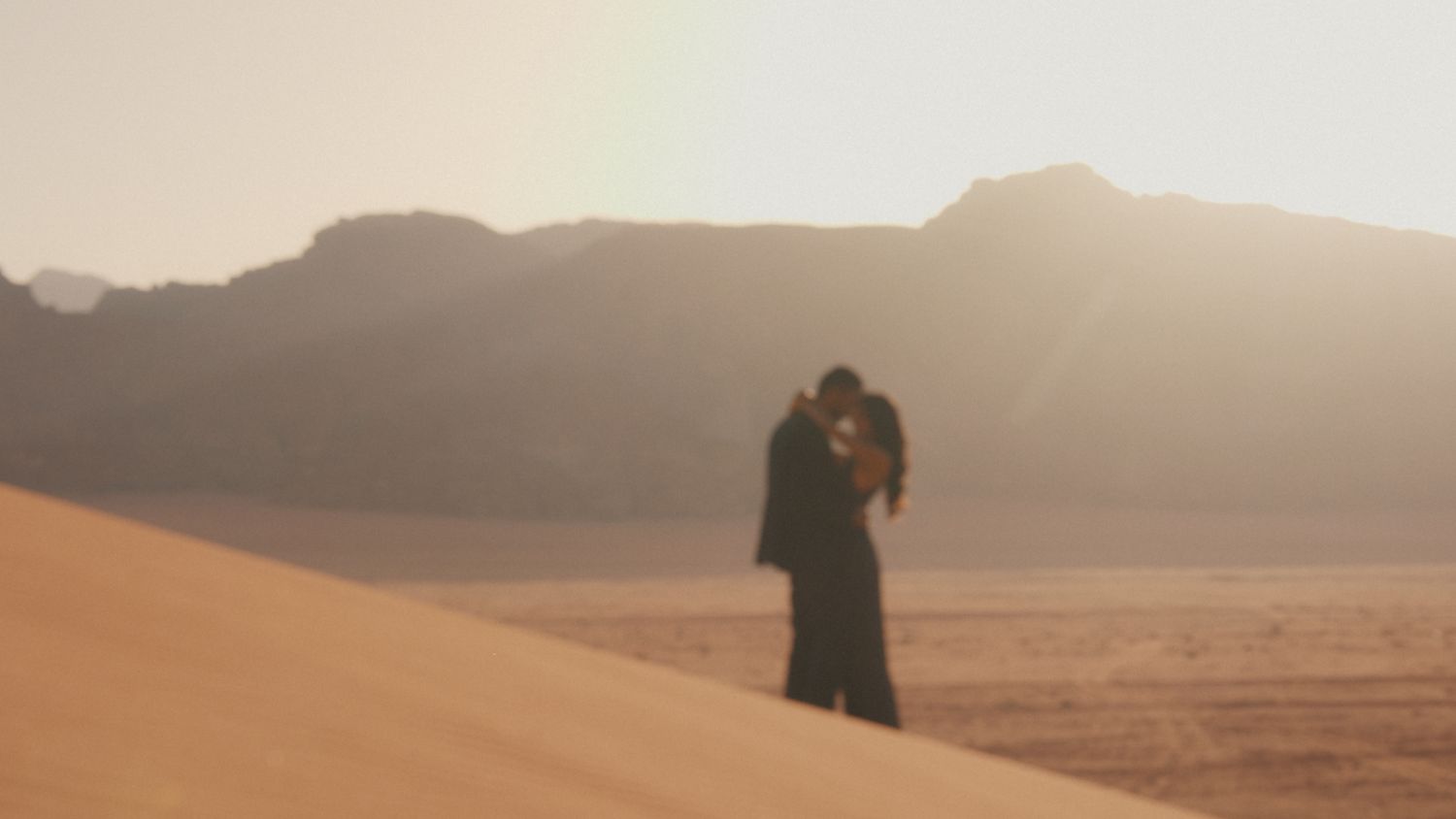 Dramatic desert landscape with mountain silhouettes at sunset.