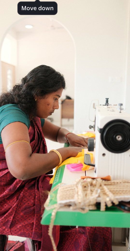 A seamstress in a red dress works diligently at a sewing machine in a bright, well-lit workspace.