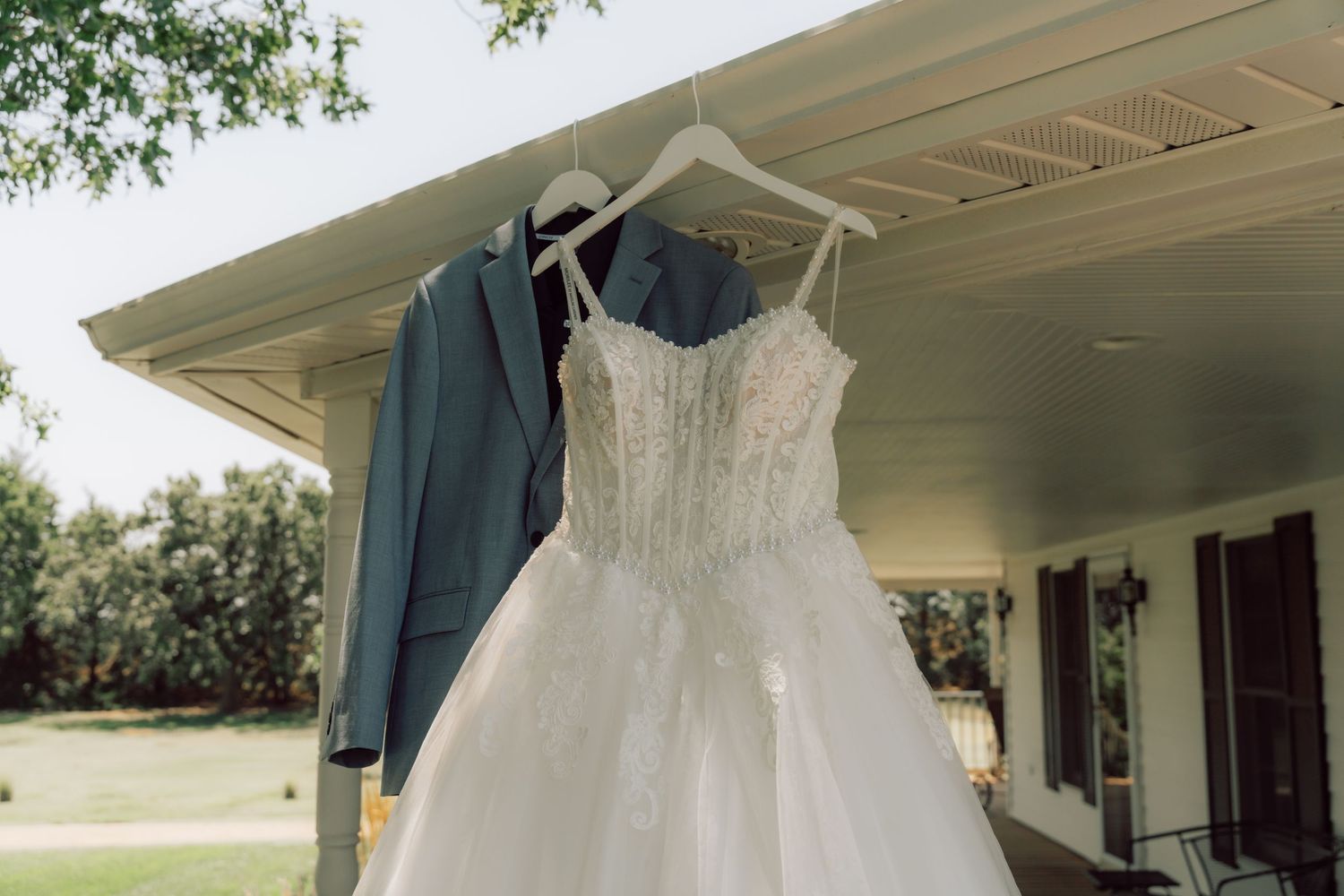 A stunning white wedding dress with intricate lace details hangs gracefully from a wooden porch railing.