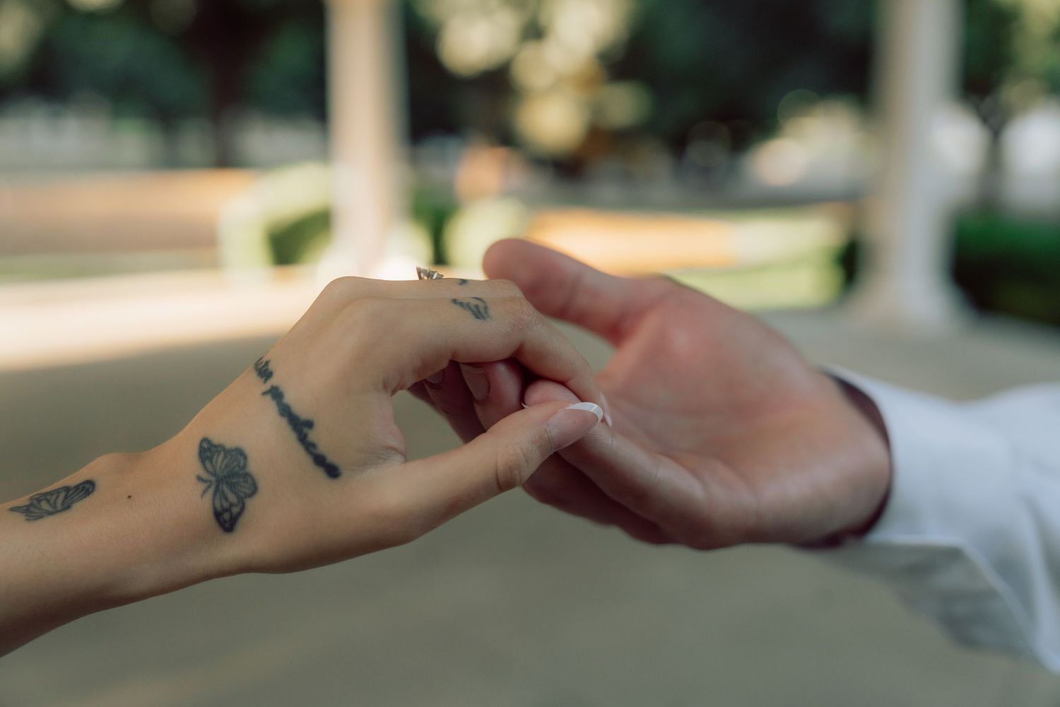 Close-up of hands with tattoos touching tenderly during a romantic moment.