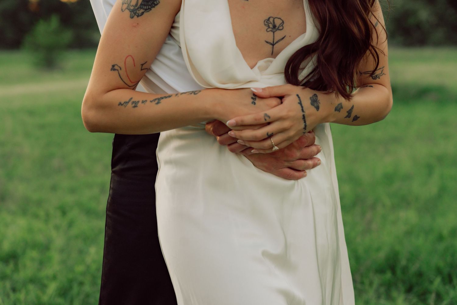 Close-up of embracing couple showing delicate floral tattoos and white wedding dress details.