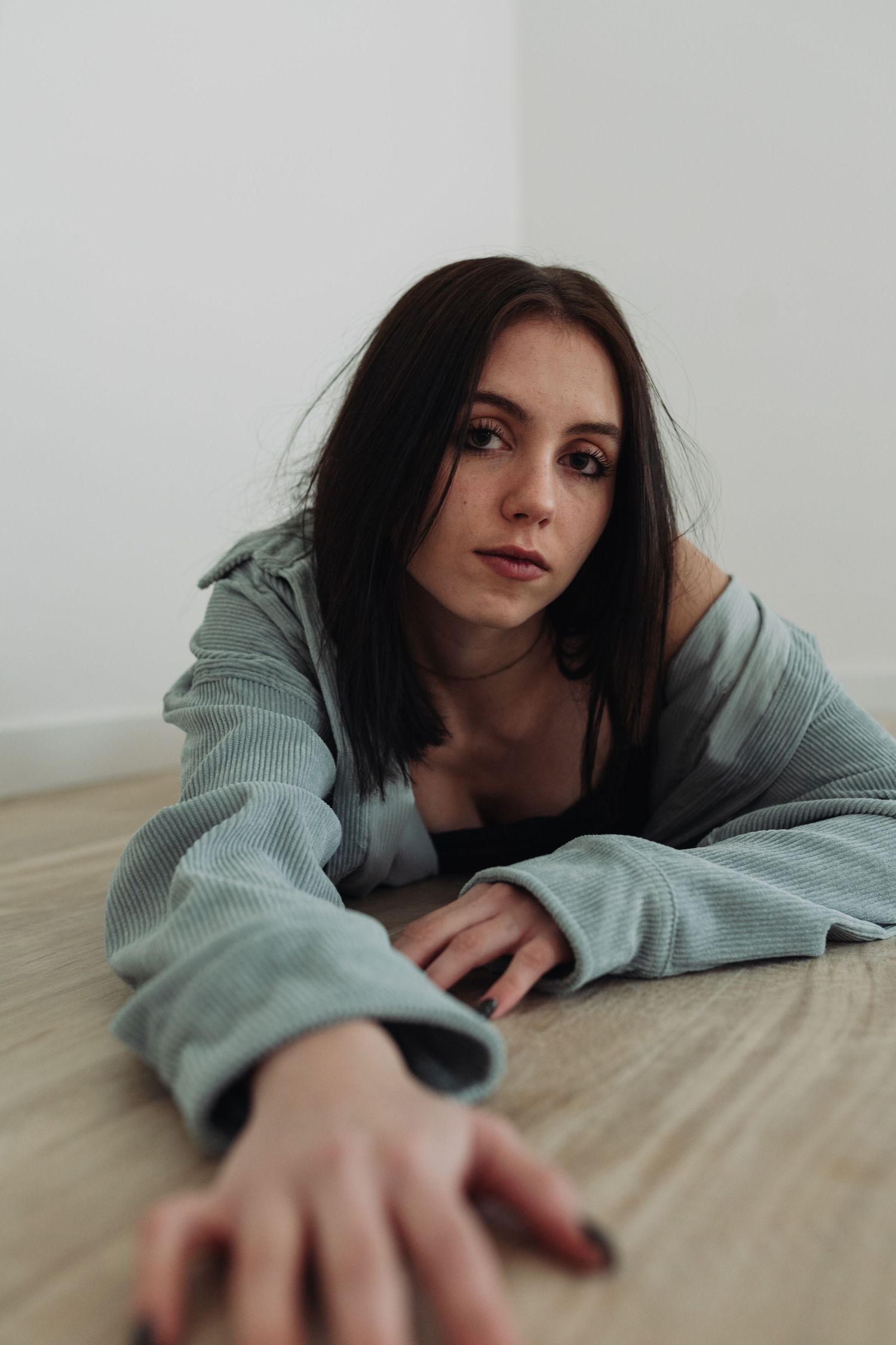 Person with dark hair in gray sweater lying on wooden floor reaching forward.