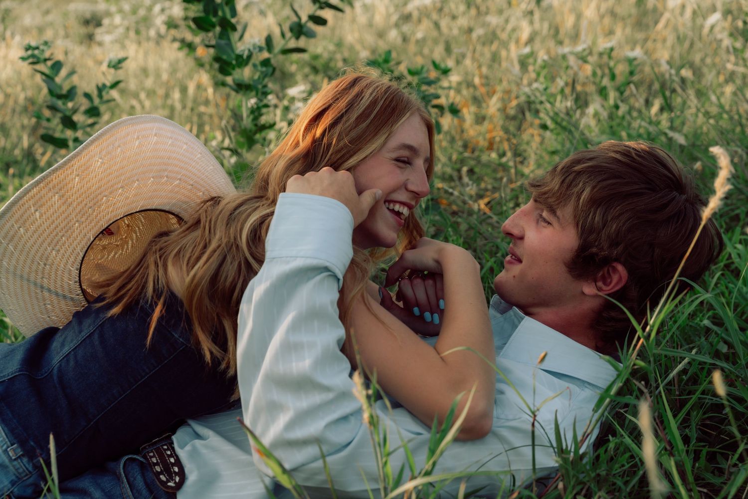 A couple laughs together while laying in a sunlit meadow.