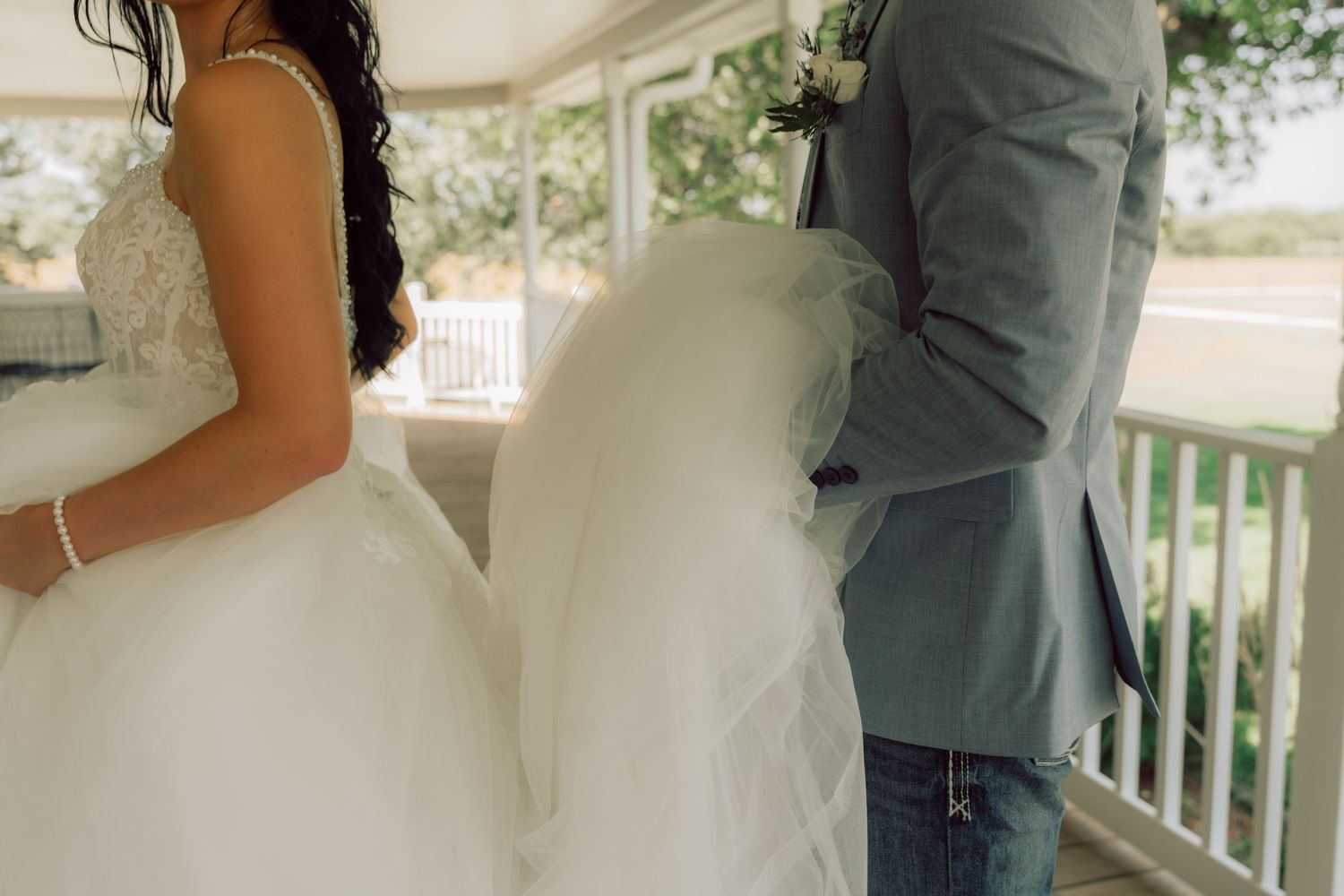 A close-up detail shot of a wedding couple's attire showing a white gown and sage green jacket.