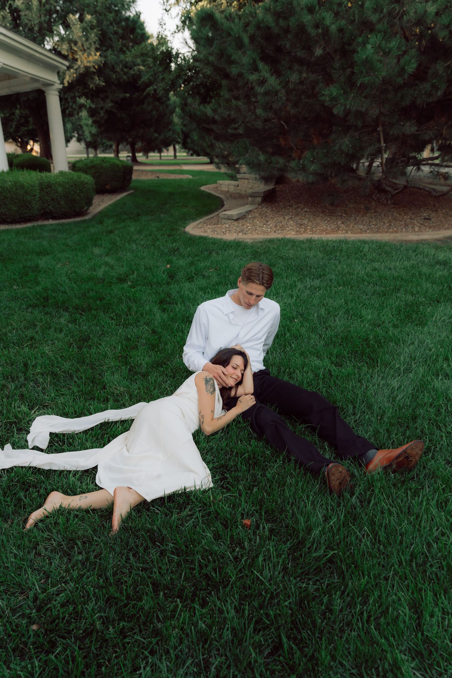 A couple in white and dark clothing lies playfully on green grass.
