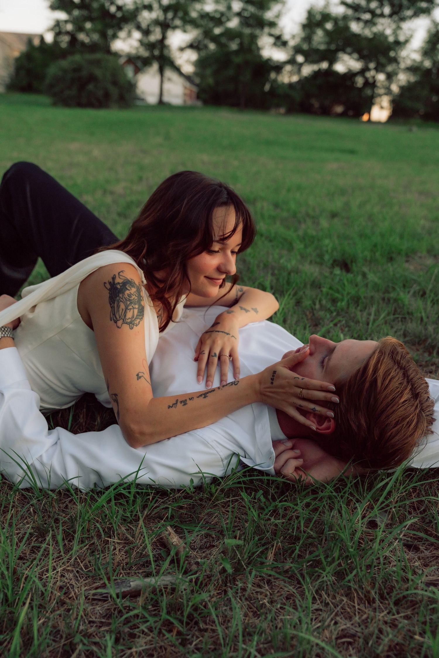 A couple lying together in a grassy field during sunset wearing white and dark clothing.