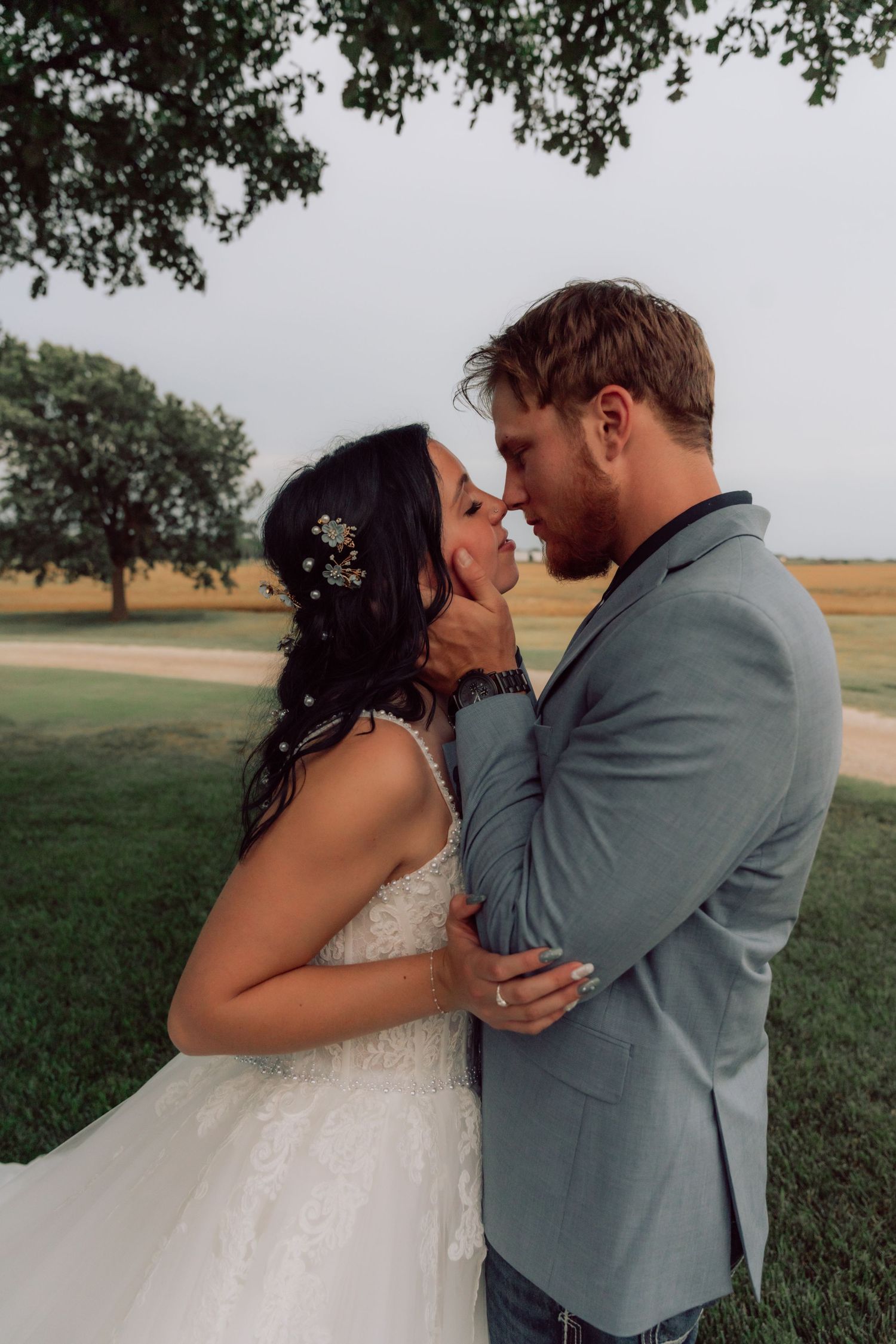 Couple shares romantic wedding photos in a rustic outdoor setting with grey skies.