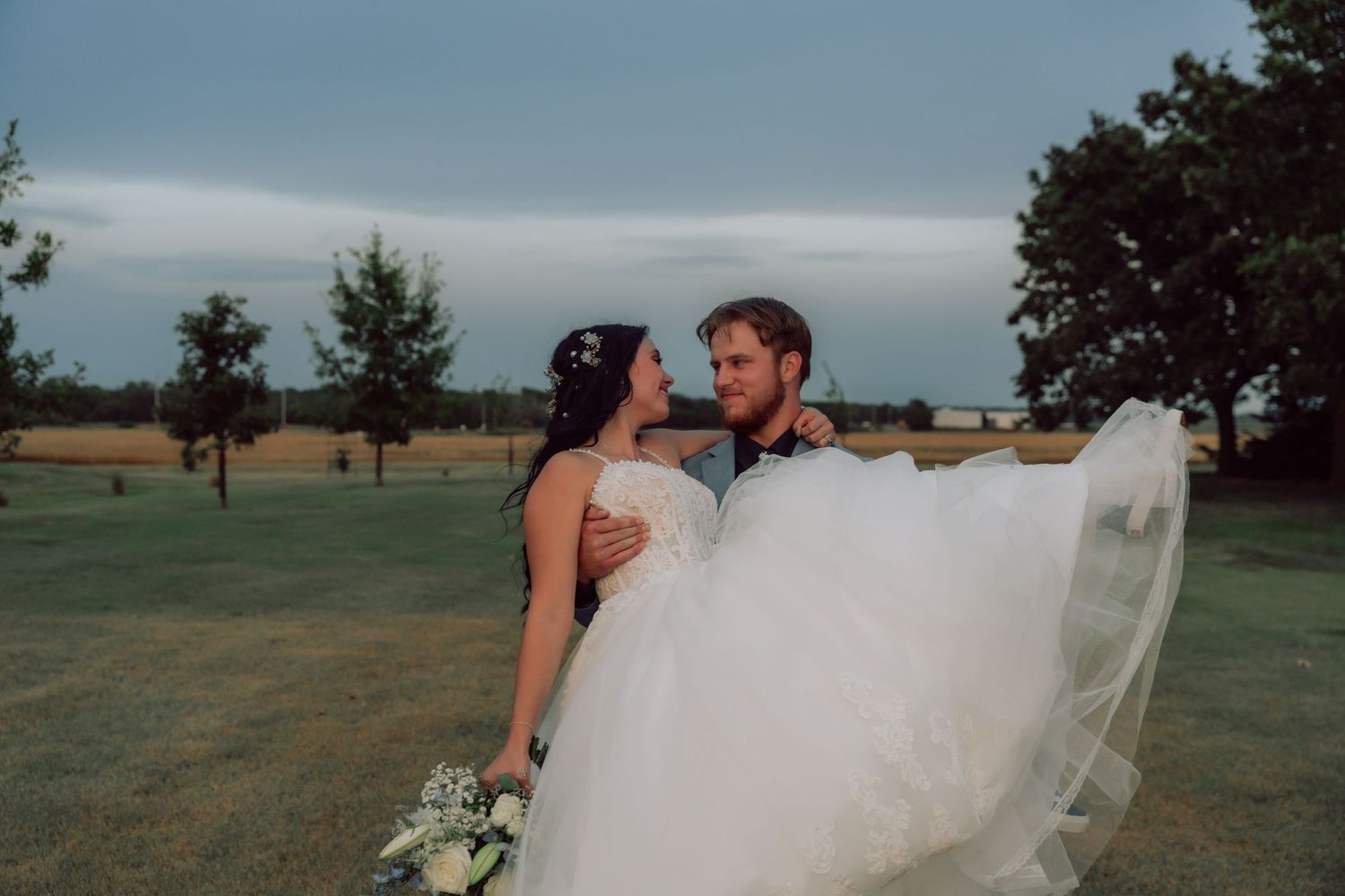 Dreamy wedding photos feature flowing white dress against pastoral landscape.
