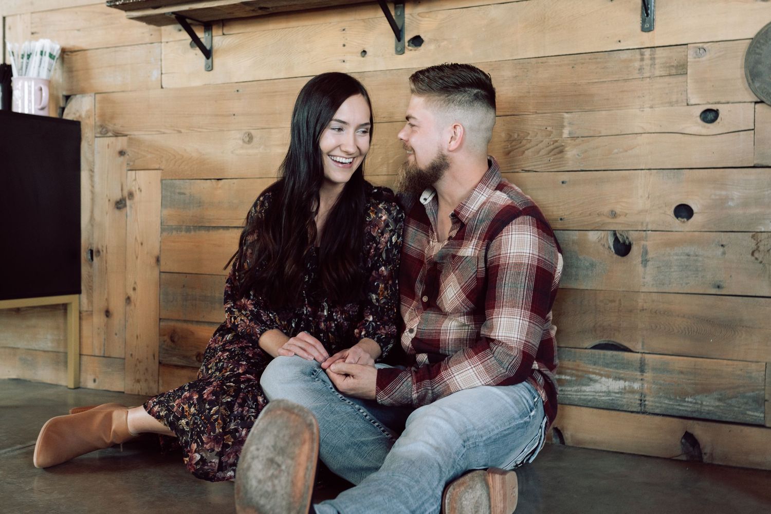 Couple sharing affectionate moments on wooden bench in rustic indoor setting.