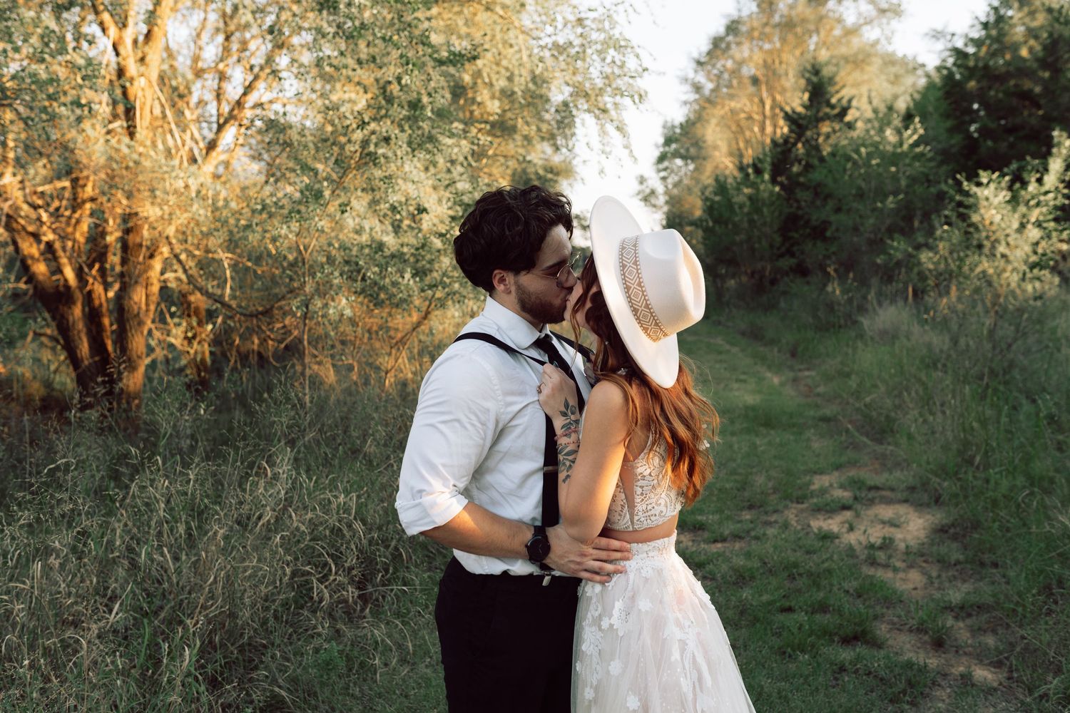 Romantic wedding photo of a couple walking along an outdoor trail at sunset.