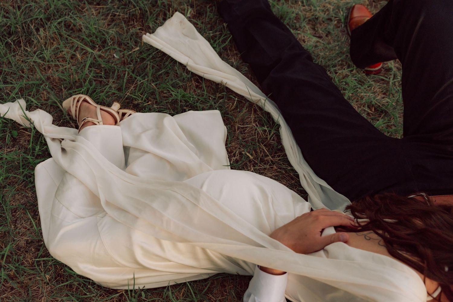 A couple in white clothing resting together on grass during golden hour.