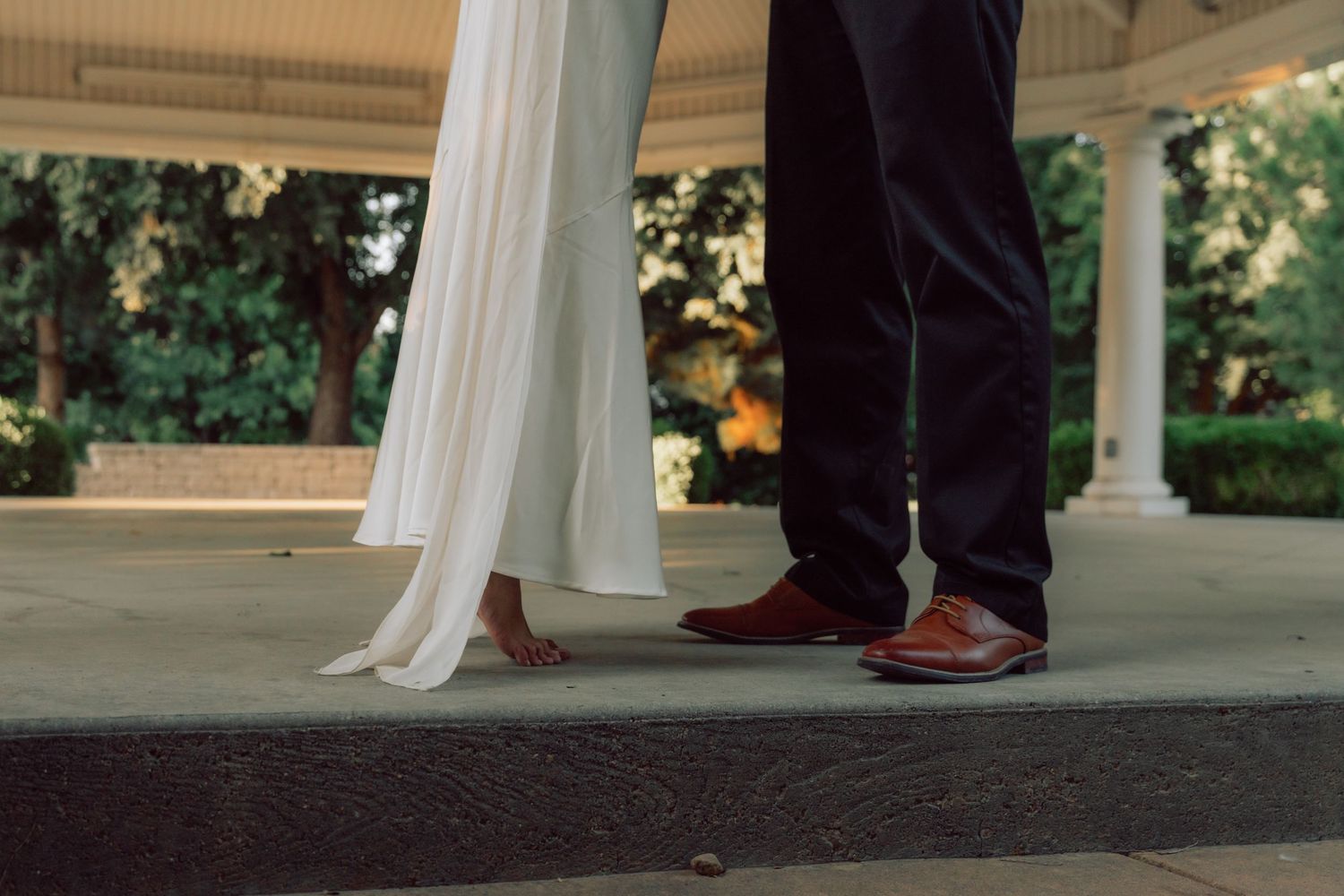 A close-up view of formal shoes and a flowing white dress on a gazebo platform.