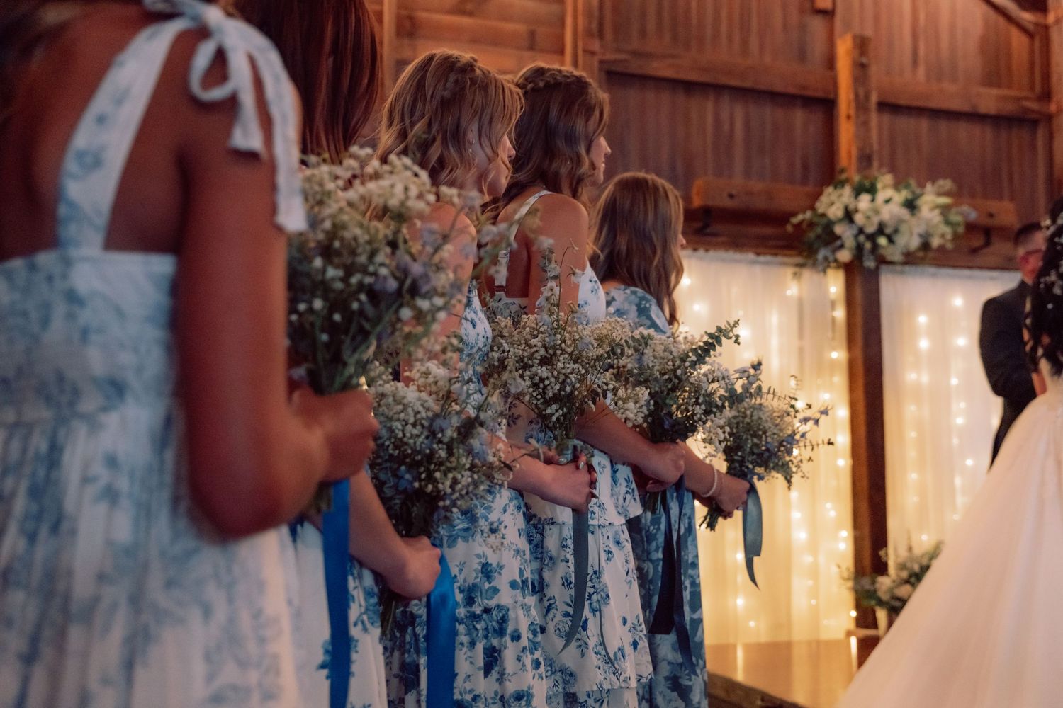 Wedding ceremony setup in a rustic wooden barn with twinkling lights and floral arrangements.