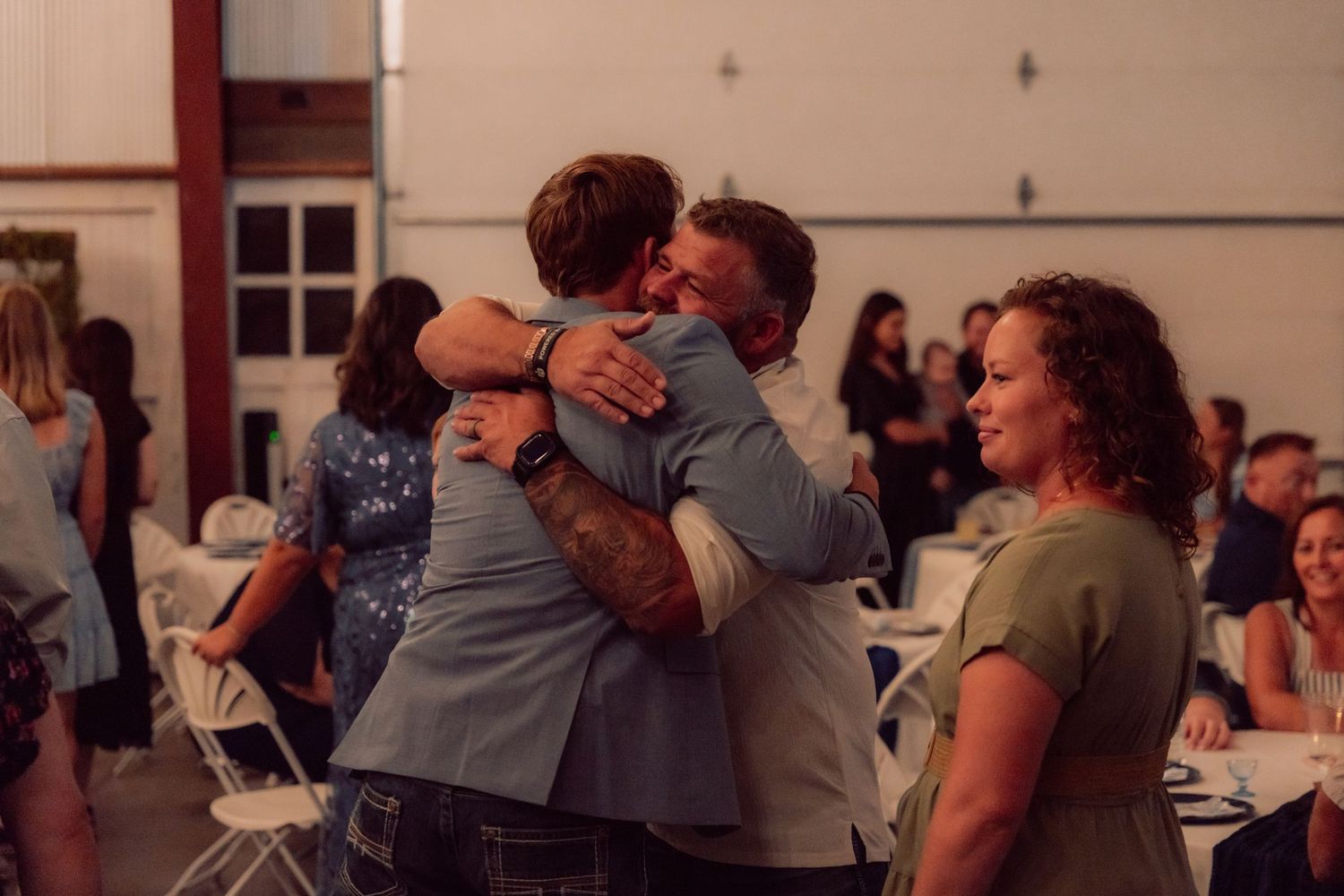 Wedding reception guests embracing and dancing in a dimly lit venue.